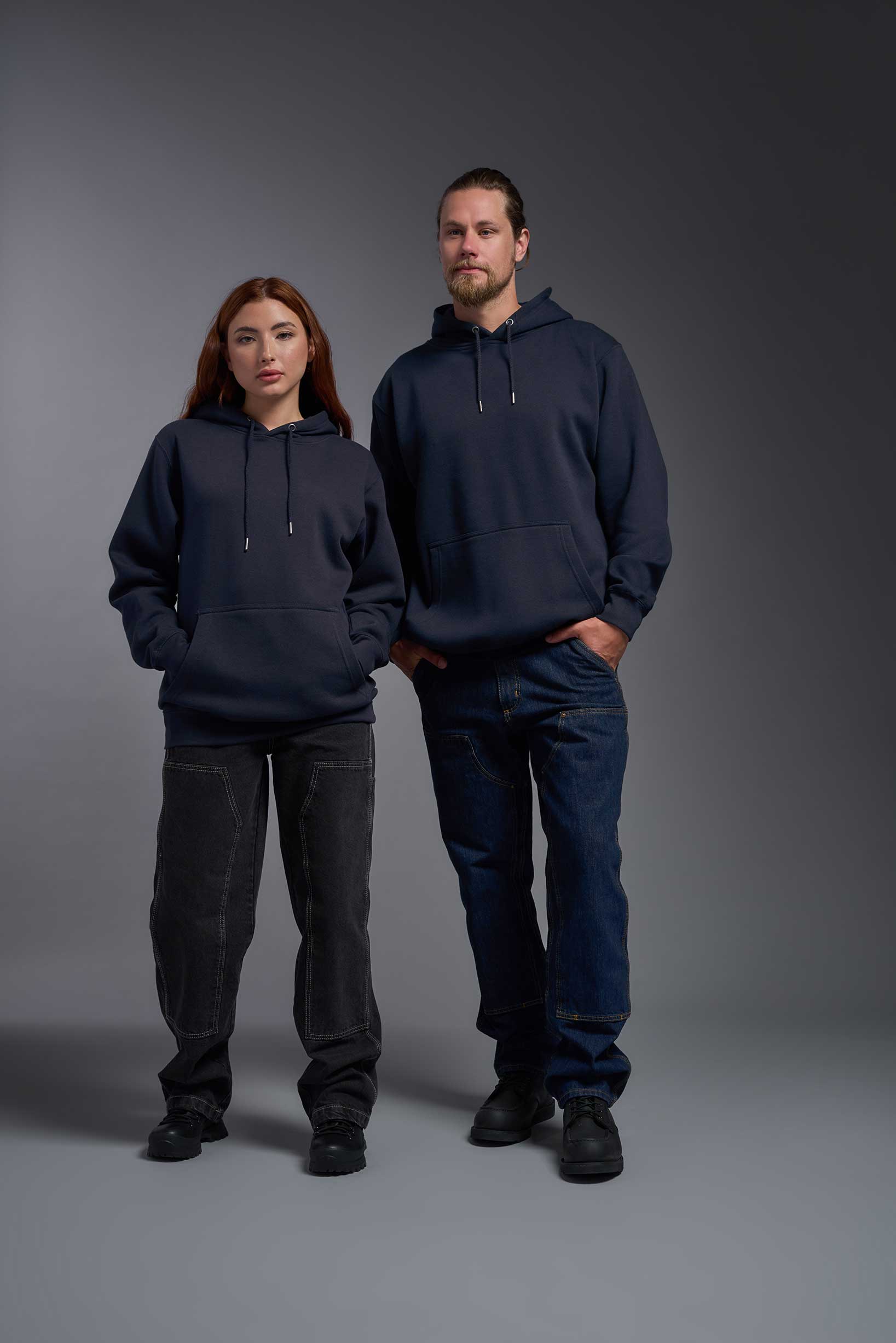 A male and female model wearing the unisex Americana 3-End Fleece Pullover Hoodie in the color navy, made from 75% combed ring-spun USA-grown cotton and 25% polyester, showing the relaxed fit from a front view. This premium fleece hoodie is Made in the USA. #navy