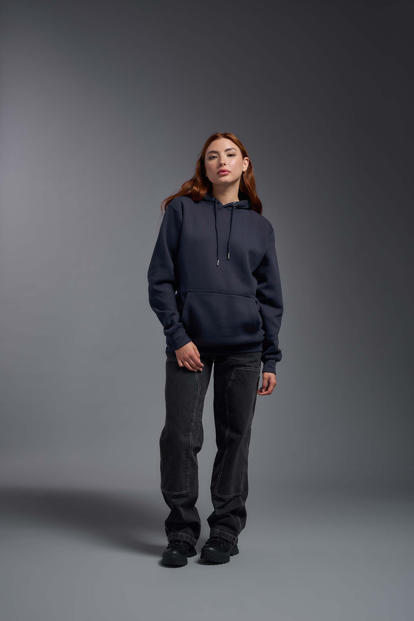 A female model wearing the unisex Americana 3-End Fleece Pullover Hoodie in the color navy, made from 75% combed ring-spun USA-grown cotton and 25% polyester, showing the relaxed fit from a front view. This premium fleece hoodie is Made in the USA. #navy