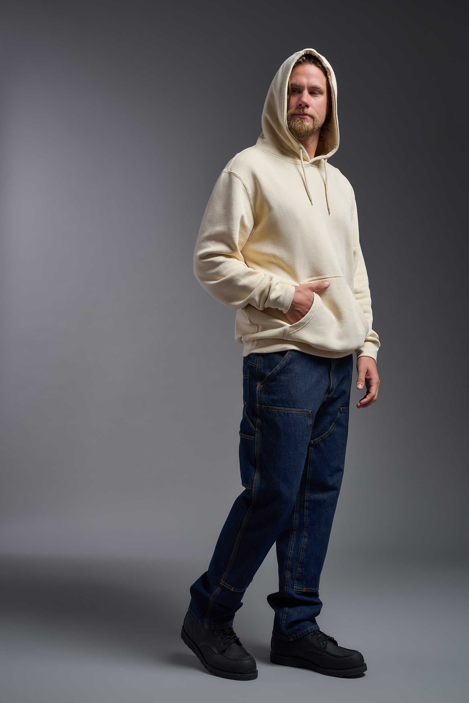 A male model wearing the unisex Americana 3-End Fleece Pullover Hoodie in the color sand, made from 75% combed ring-spun USA-grown cotton and 25% polyester, showing the relaxed fit from a front view with hood up. This premium fleece hoodie is Made in the USA. #sand