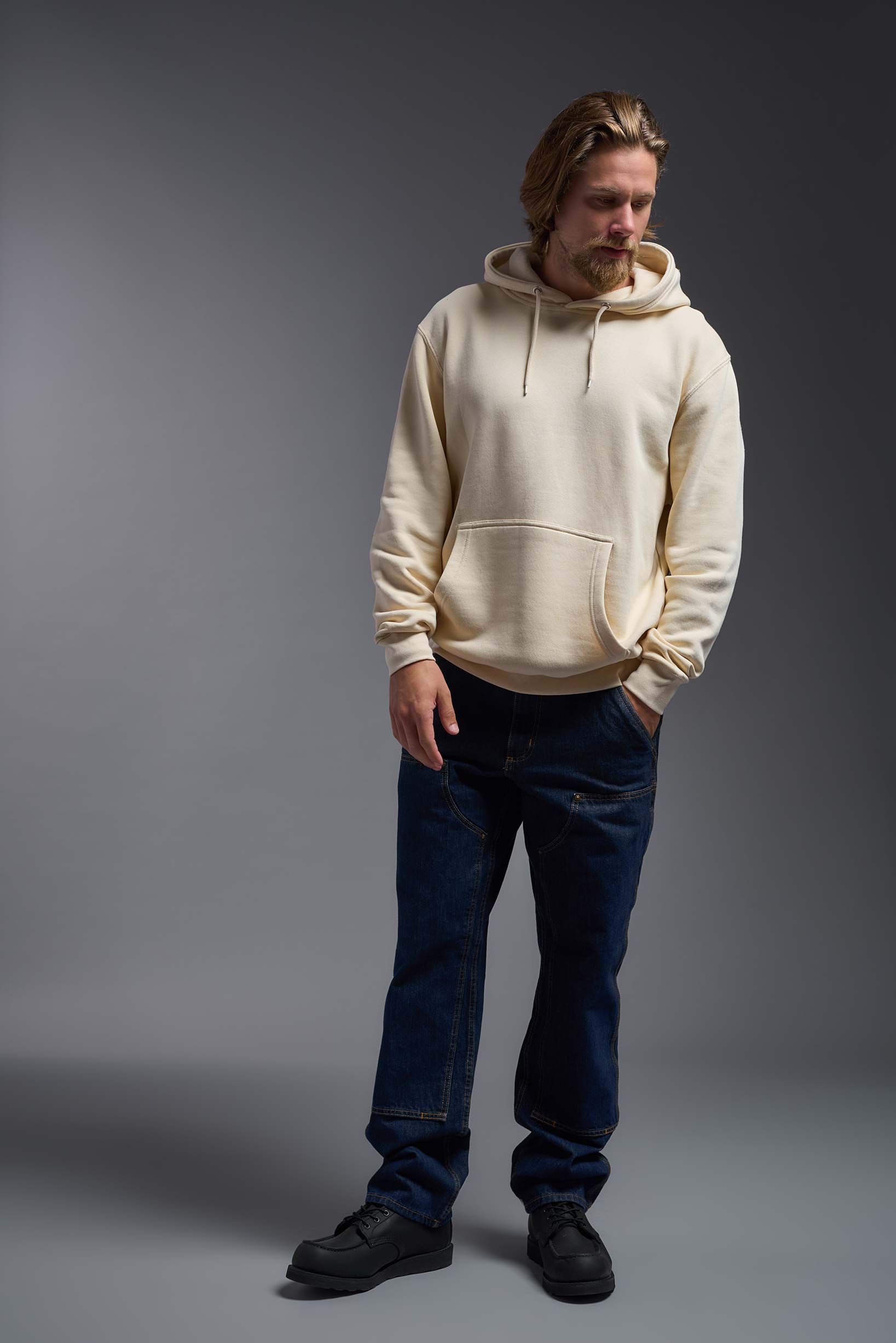 A male model wearing the unisex Americana 3-End Fleece Pullover Hoodie in the color sand, made from 75% combed ring-spun USA-grown cotton and 25% polyester, showing the relaxed fit from a front view. This premium fleece hoodie is Made in the USA. #sand