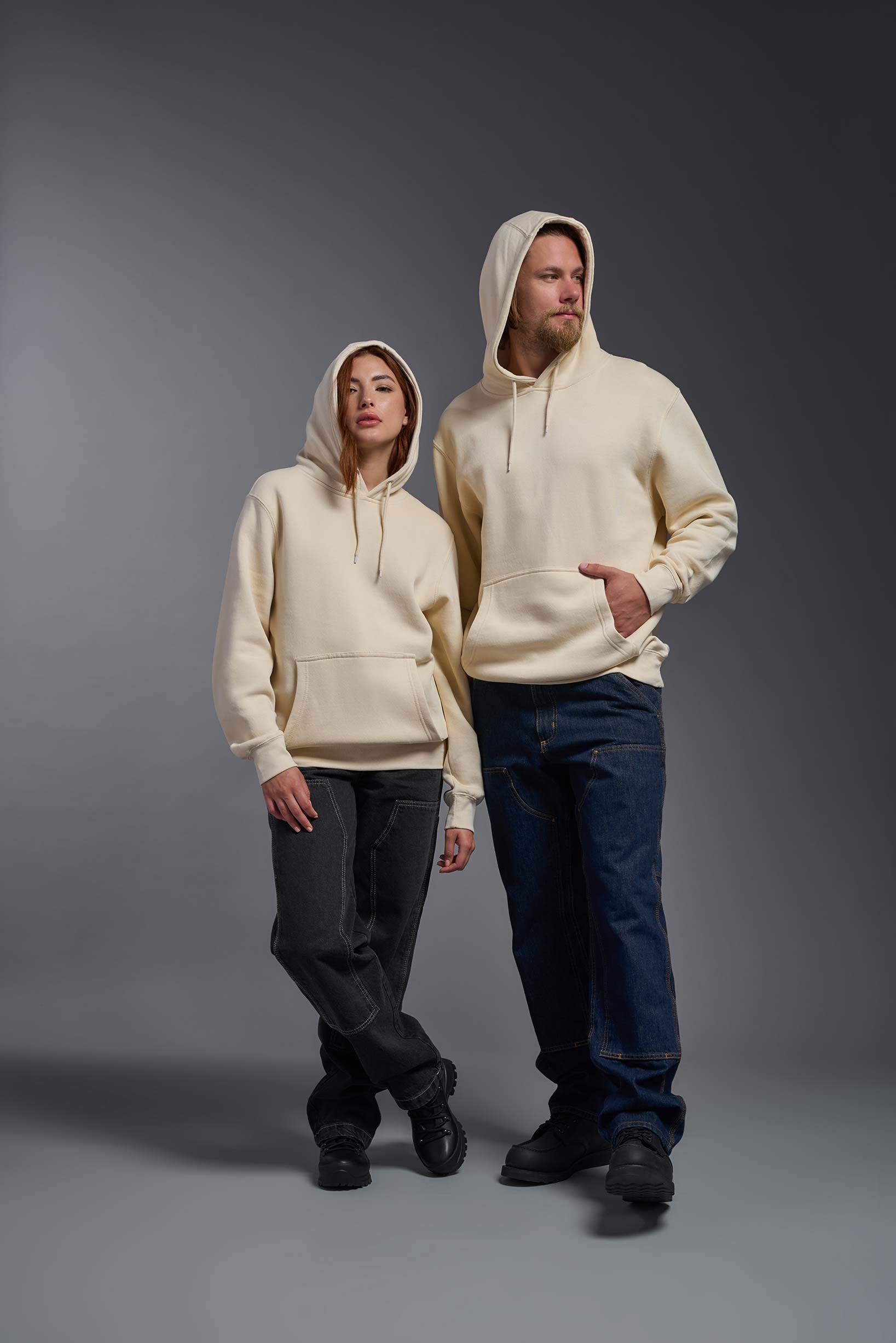 A male and female model wearing the unisex Americana 3-End Fleece Pullover Hoodie in the color sand, made from 75% combed ring-spun USA-grown cotton and 25% polyester, showing the relaxed fit from a front view with hoods up. This premium fleece hoodie is Made in the USA. #sand