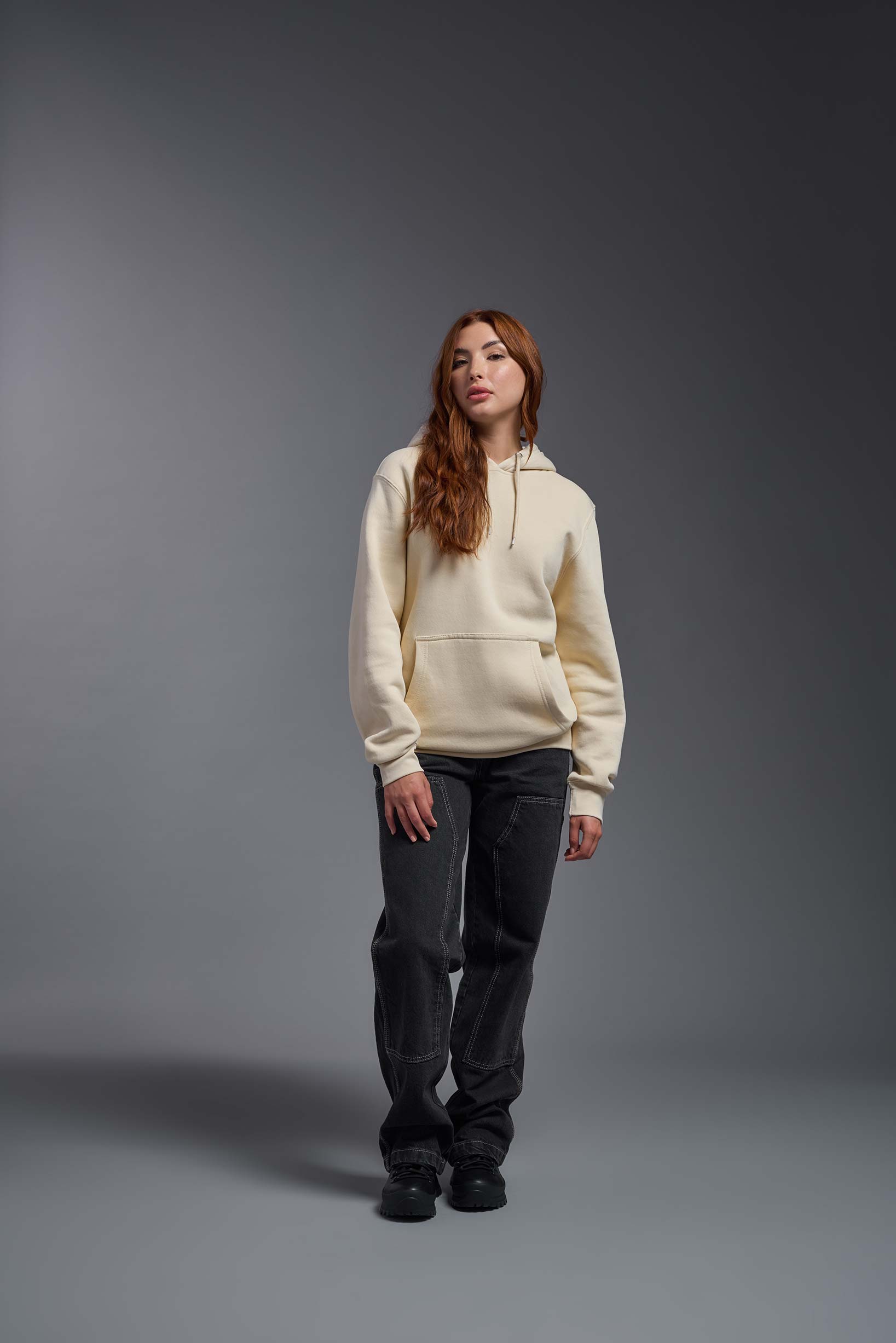 A female model wearing the unisex Americana 3-End Fleece Pullover Hoodie in the color sand, made from 75% combed ring-spun USA-grown cotton and 25% polyester, showing the relaxed fit from a front view. This premium fleece hoodie is Made in the USA. #sand