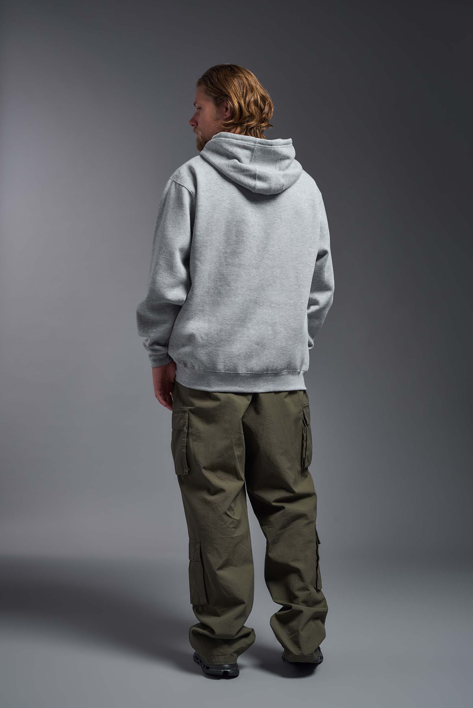 A male model wearing the unisex Americana 3-End Fleece Pullover Hoodie in the color sport gray, made from 75% combed ring-spun USA-grown cotton and 25% polyester, showing the relaxed fit from a back view. This premium fleece hoodie is Made in the USA. #sport-gray