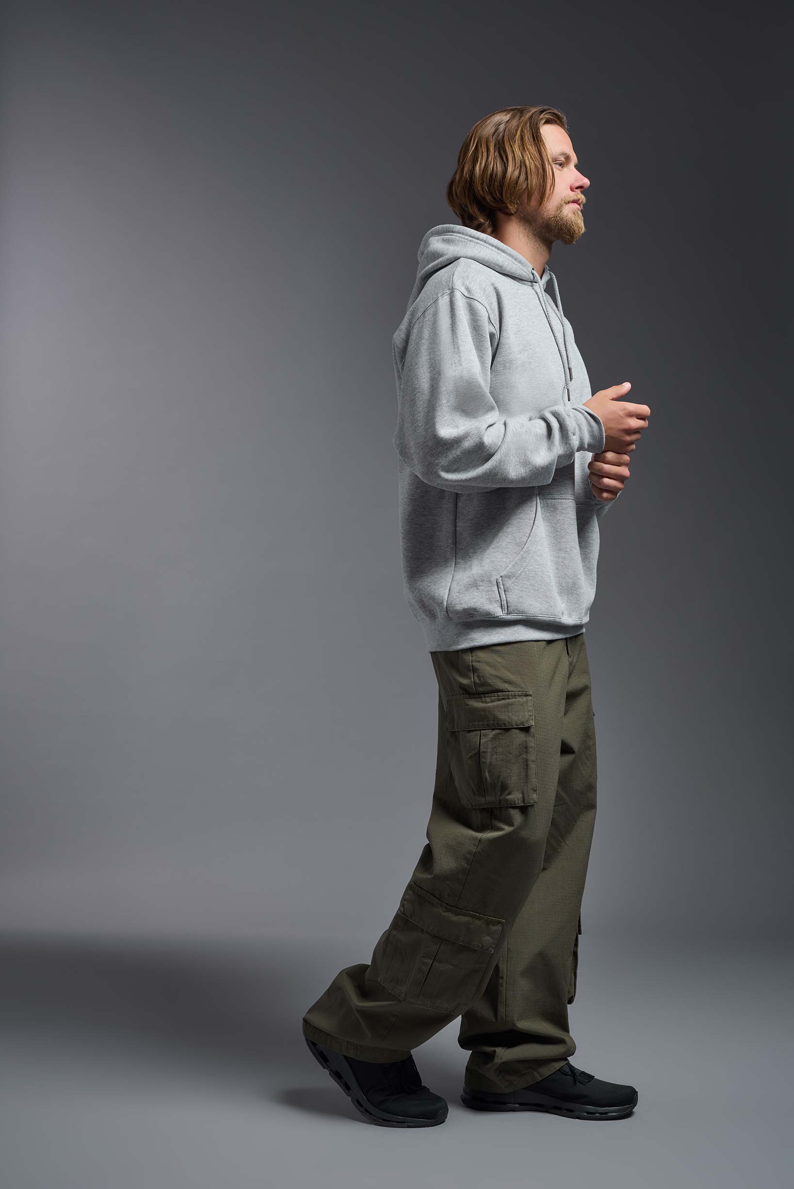 A male model wearing the unisex Americana 3-End Fleece Pullover Hoodie in the color sport gray, made from 75% combed ring-spun USA-grown cotton and 25% polyester, showing the relaxed fit from a side view. This premium fleece hoodie is Made in the USA. #sport-gray