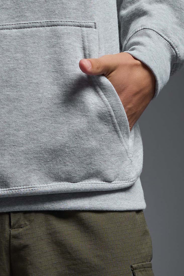 A male model wearing the unisex Americana 3-End Fleece Pullover Hoodie in the color sport gray, made from 75% combed ring-spun USA-grown cotton and 25% polyester, showing the relaxed fit from a close-up pocket view. This premium fleece hoodie is Made in the USA. #sport-gray