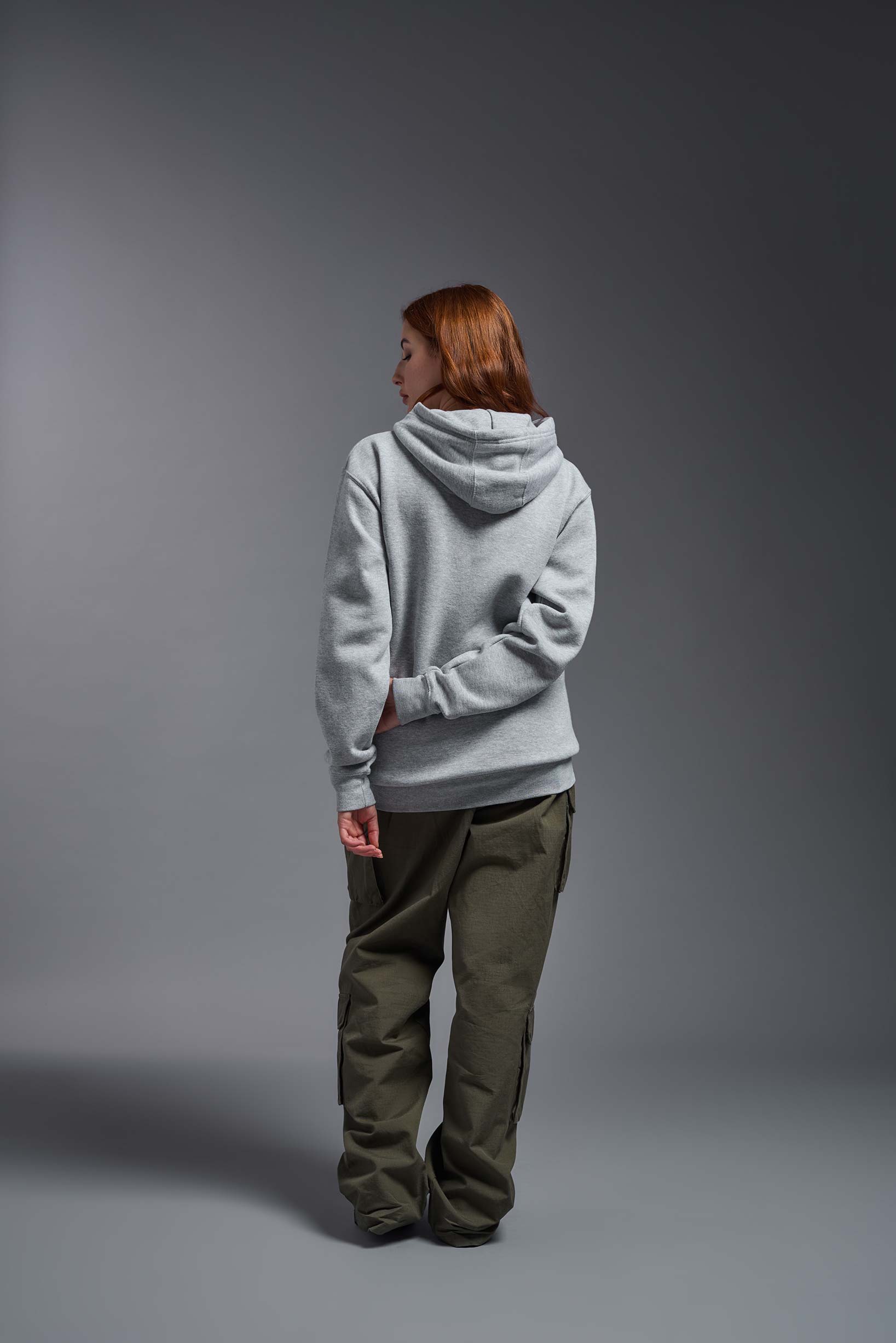 A female model wearing the unisex Americana 3-End Fleece Pullover Hoodie in the color sport gray, made from 75% combed ring-spun USA-grown cotton and 25% polyester, showing the relaxed fit from a back view. This premium fleece hoodie is Made in the USA. #sport-gray