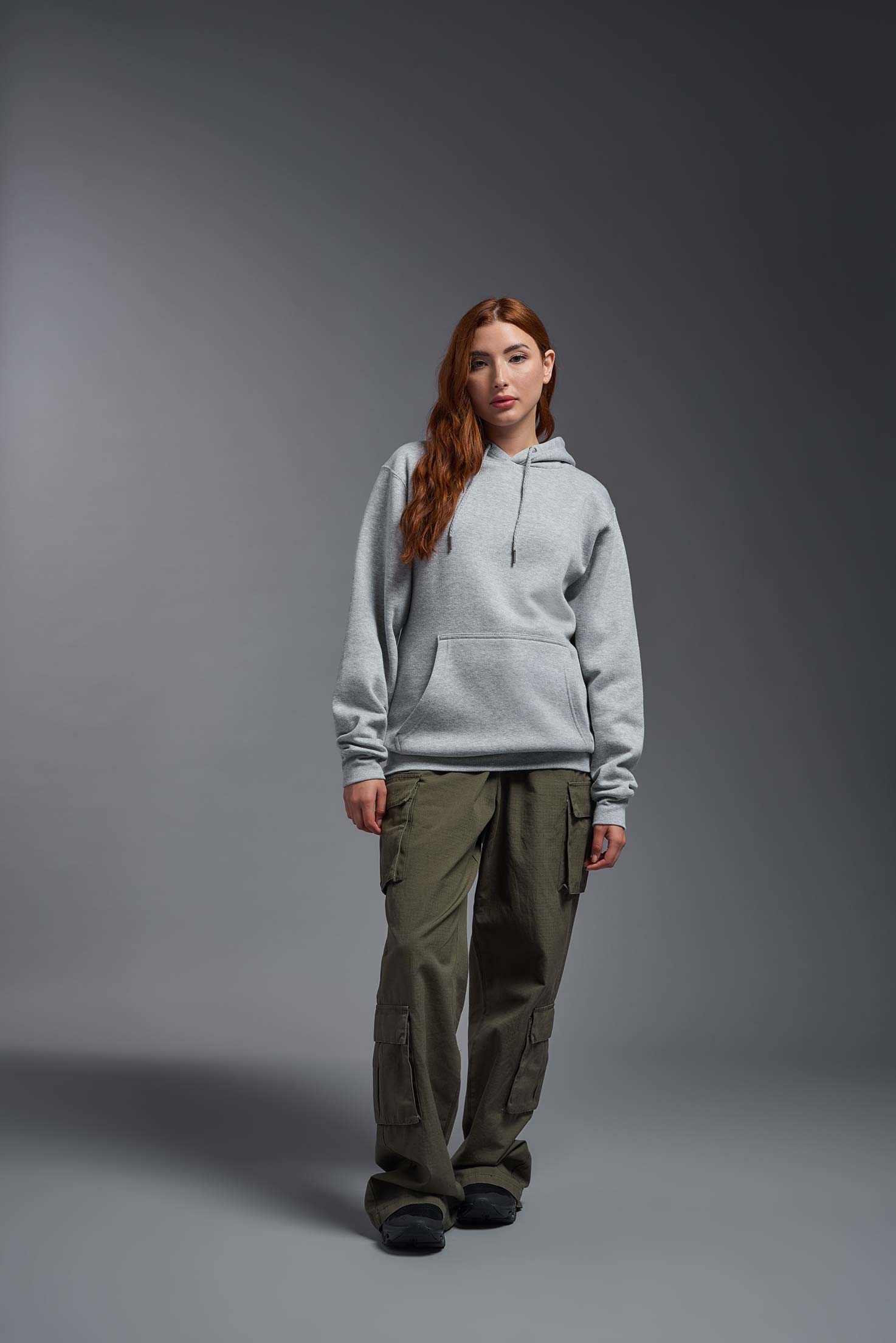 A female model wearing the unisex Americana 3-End Fleece Pullover Hoodie in the color sport gray, made from 75% combed ring-spun USA-grown cotton and 25% polyester, showing the relaxed fit from a front view. This premium fleece hoodie is Made in the USA. #sport-gray