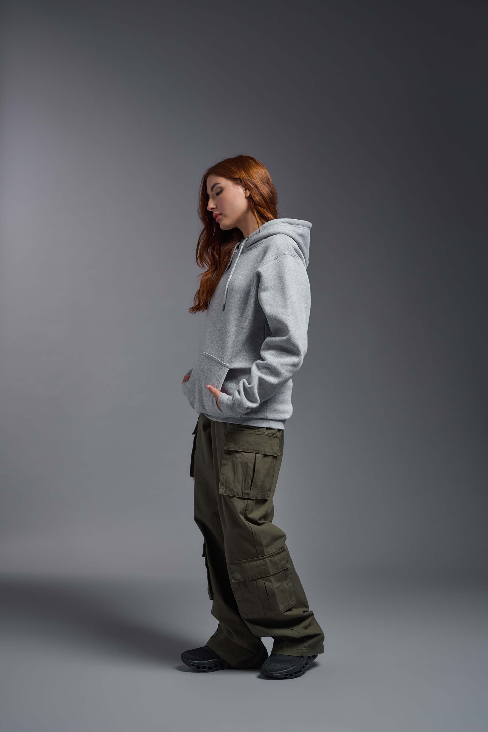A female model wearing the unisex Americana 3-End Fleece Pullover Hoodie in the color sport gray, made from 75% combed ring-spun USA-grown cotton and 25% polyester, showing the relaxed fit from a side view. This premium fleece hoodie is Made in the USA. #sport-gray