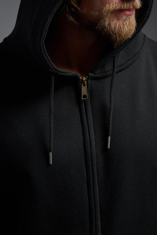 A male model wearing the unisex Americana 3-End Fleece Full Zip Hoodie in the color black, made from 75% combed ring-spun USA-grown cotton and 25% polyester, showing the relaxed fit from a collar close-up view. This premium fleece hoodie is Made in the USA. #black