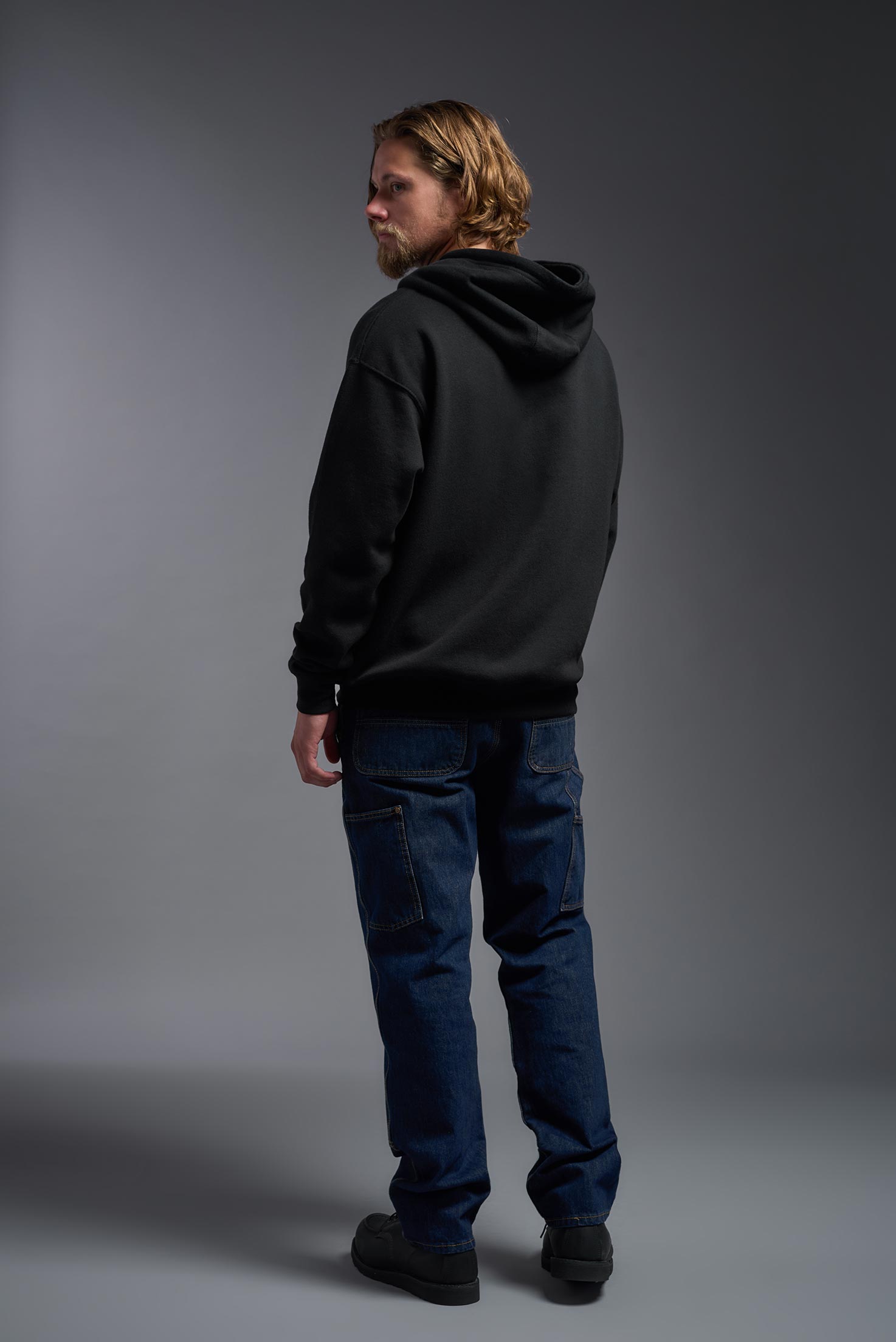 A male model wearing the unisex Americana 3-End Fleece Full Zip Hoodie in the color black, made from 75% combed ring-spun USA-grown cotton and 25% polyester, showing the relaxed fit from a back view. This premium fleece hoodie is Made in the USA. #black