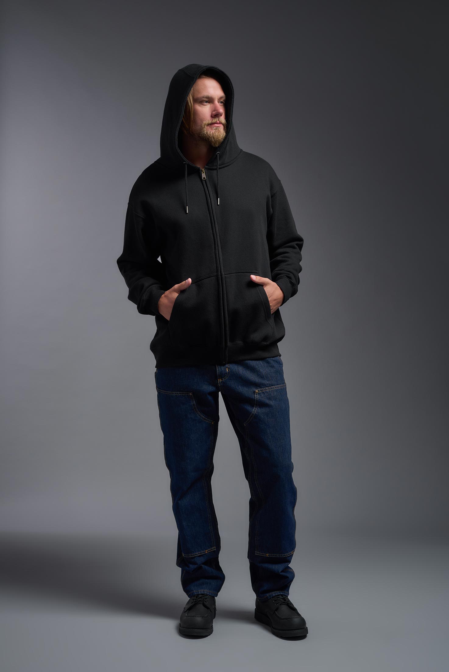 A male model wearing the unisex Americana 3-End Fleece Full Zip Hoodie in the color black, made from 75% combed ring-spun USA-grown cotton and 25% polyester, showing the relaxed fit from a front view with the hood up. This premium fleece hoodie is Made in the USA. #black
