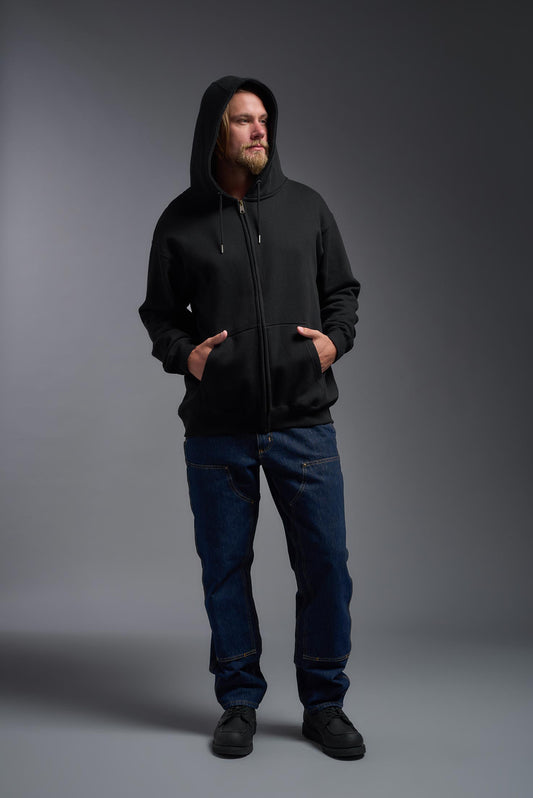 A male model wearing the unisex Americana 3-End Fleece Full Zip Hoodie in the color black, made from 75% combed ring-spun USA-grown cotton and 25% polyester, showing the relaxed fit from a front view with the hood up. This premium fleece hoodie is Made in the USA. #black