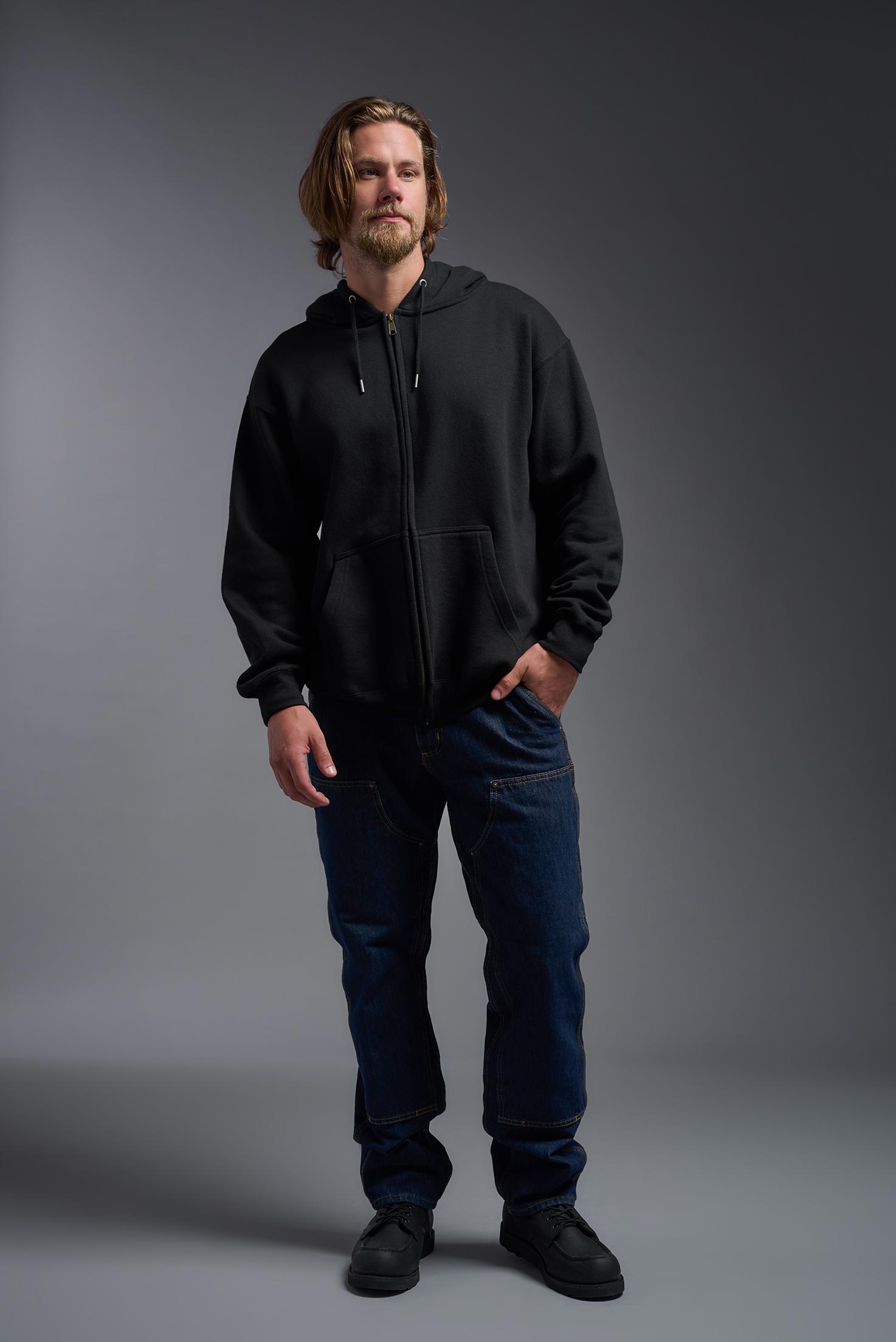 A male model wearing the unisex Americana 3-End Fleece Full Zip Hoodie in the color black, made from 75% combed ring-spun USA-grown cotton and 25% polyester, showing the relaxed fit from a front view. This premium fleece hoodie is Made in the USA. #black