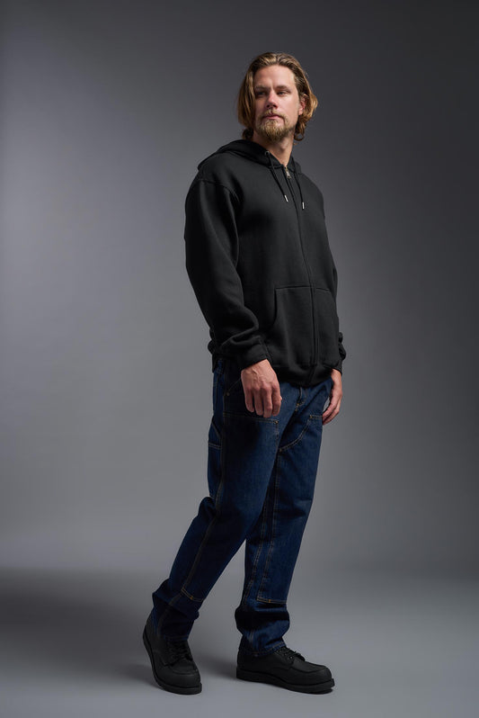 A male model wearing the unisex Americana 3-End Fleece Full Zip Hoodie in the color black, made from 75% combed ring-spun USA-grown cotton and 25% polyester, showing the relaxed fit from a side view. This premium fleece hoodie is Made in the USA. #black
