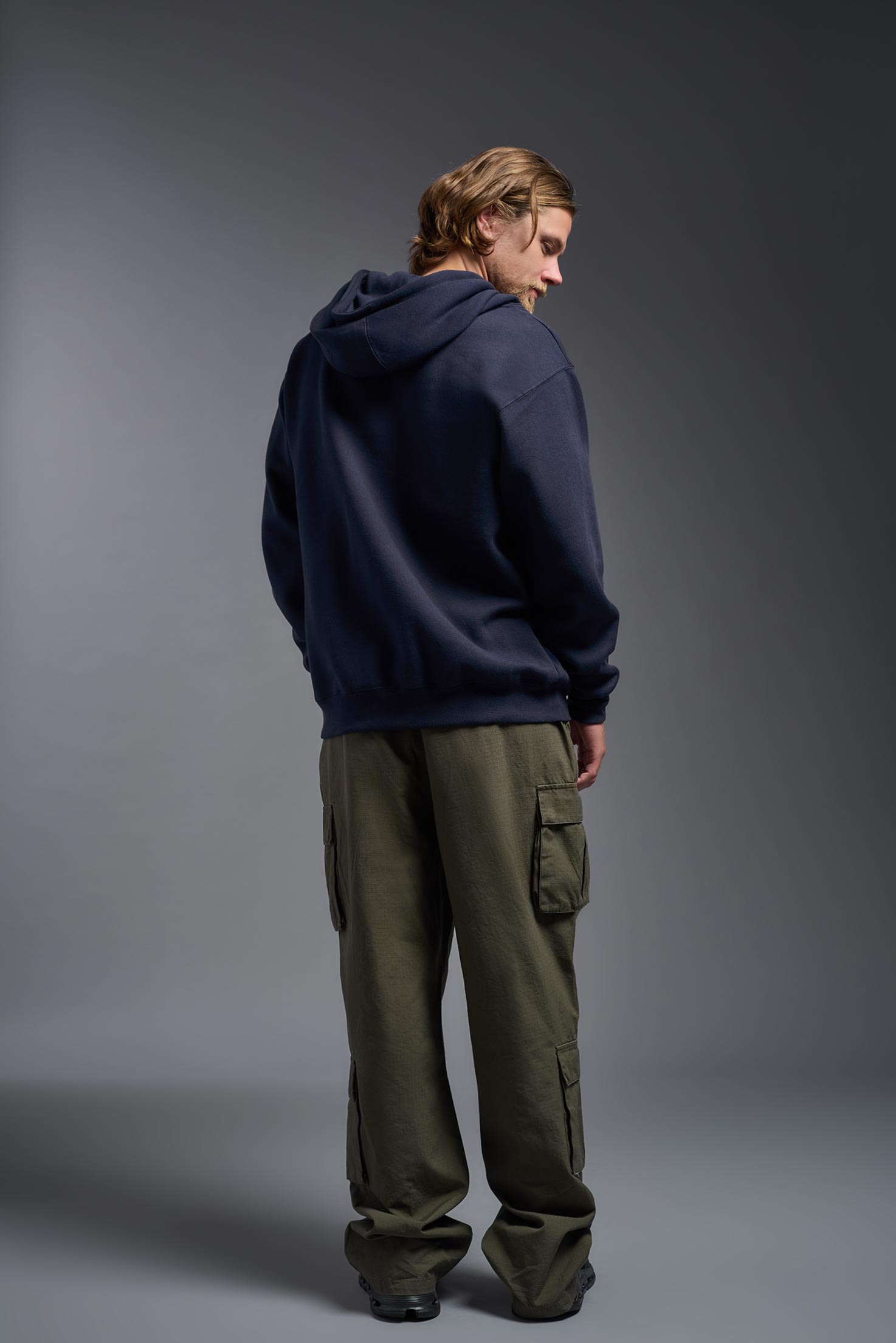A male model wearing the unisex Americana 3-End Fleece Full Zip Hoodie in the color navy, made from 75% combed ring-spun USA-grown cotton and 25% polyester, showing the relaxed fit from a back view. This premium fleece hoodie is Made in the USA. #navy