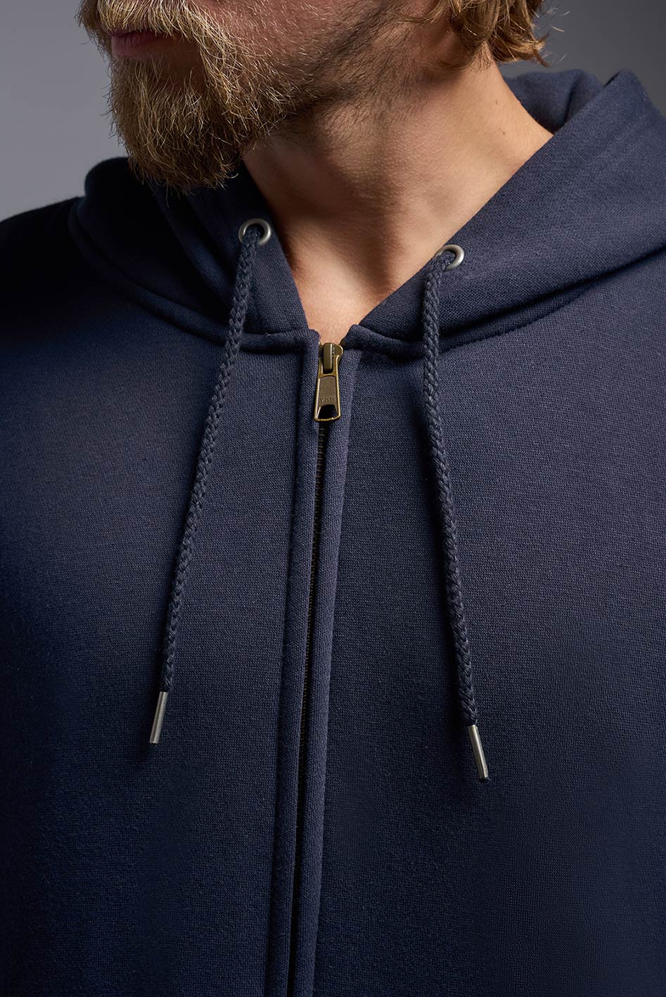 A male model wearing the unisex Americana 3-End Fleece Full Zip Hoodie in the color navy, made from 75% combed ring-spun USA-grown cotton and 25% polyester, showing the relaxed fit from a collar zipper view. This premium fleece hoodie is Made in the USA. #navy