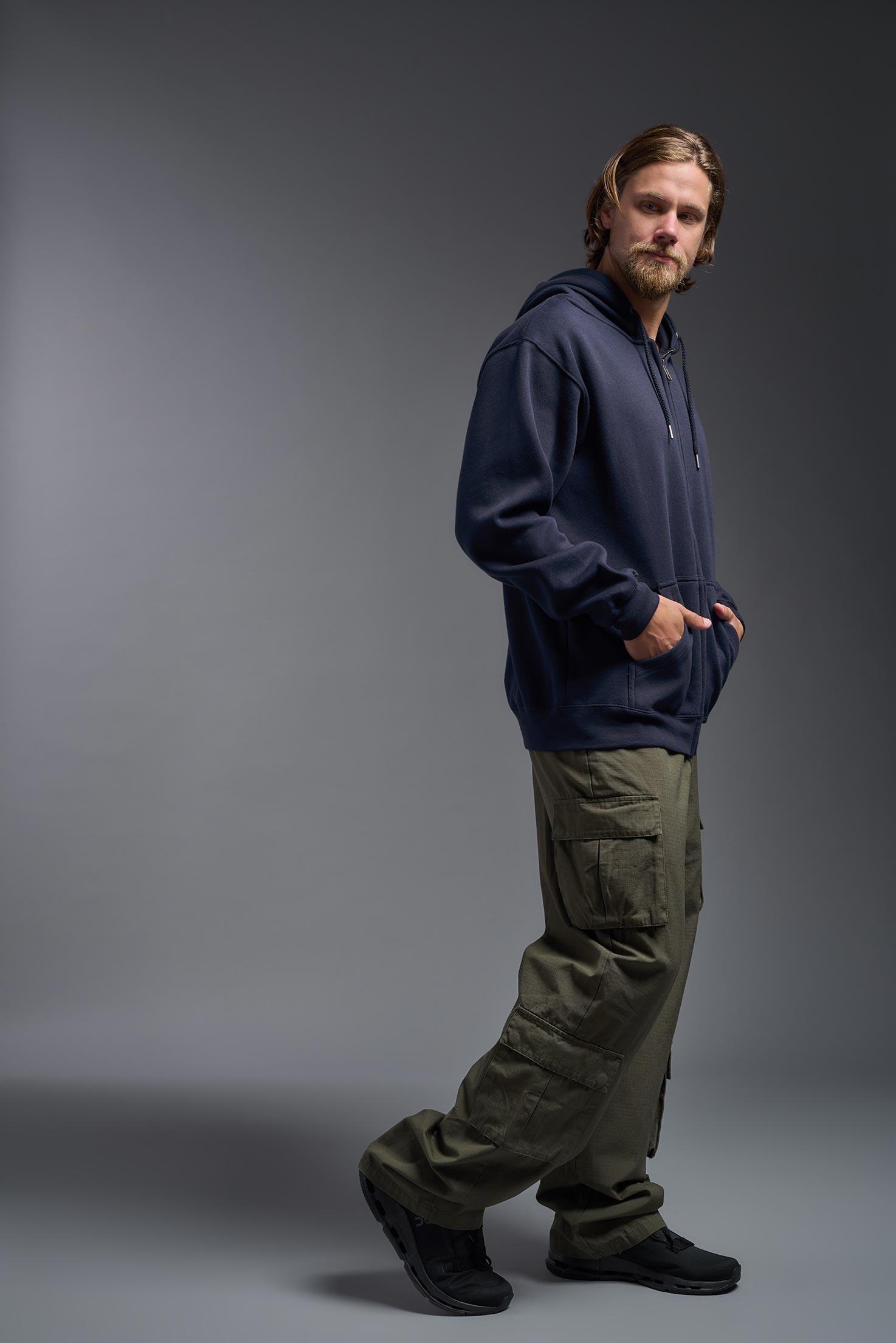 A male model wearing the unisex Americana 3-End Fleece Full Zip Hoodie in the color navy, made from 75% combed ring-spun USA-grown cotton and 25% polyester, showing the relaxed fit from a side view. This premium fleece hoodie is Made in the USA. #navy