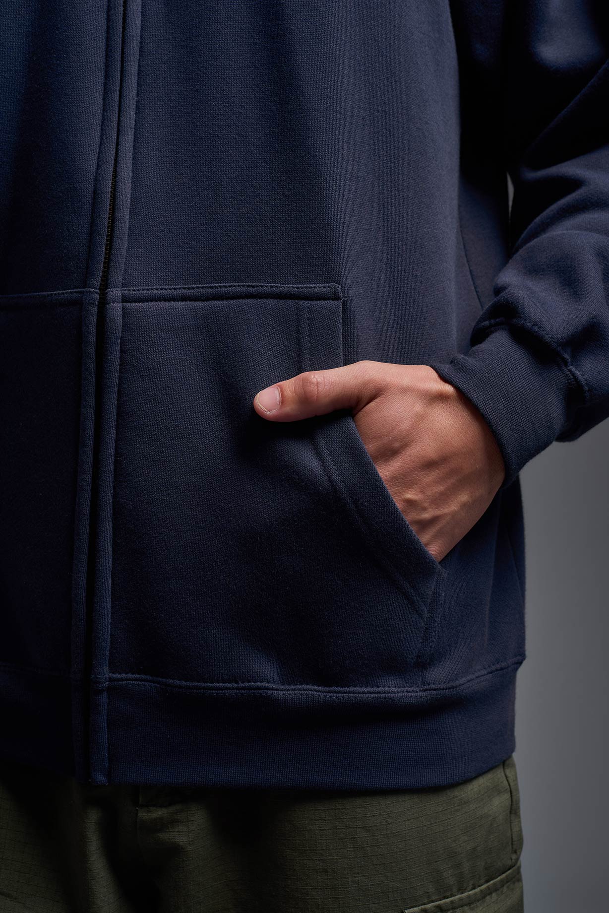 A male model wearing the unisex Americana 3-End Fleece Full Zip Hoodie in the color navy, made from 75% combed ring-spun USA-grown cotton and 25% polyester, showing the relaxed fit from a pocket view. This premium fleece hoodie is Made in the USA. #navy