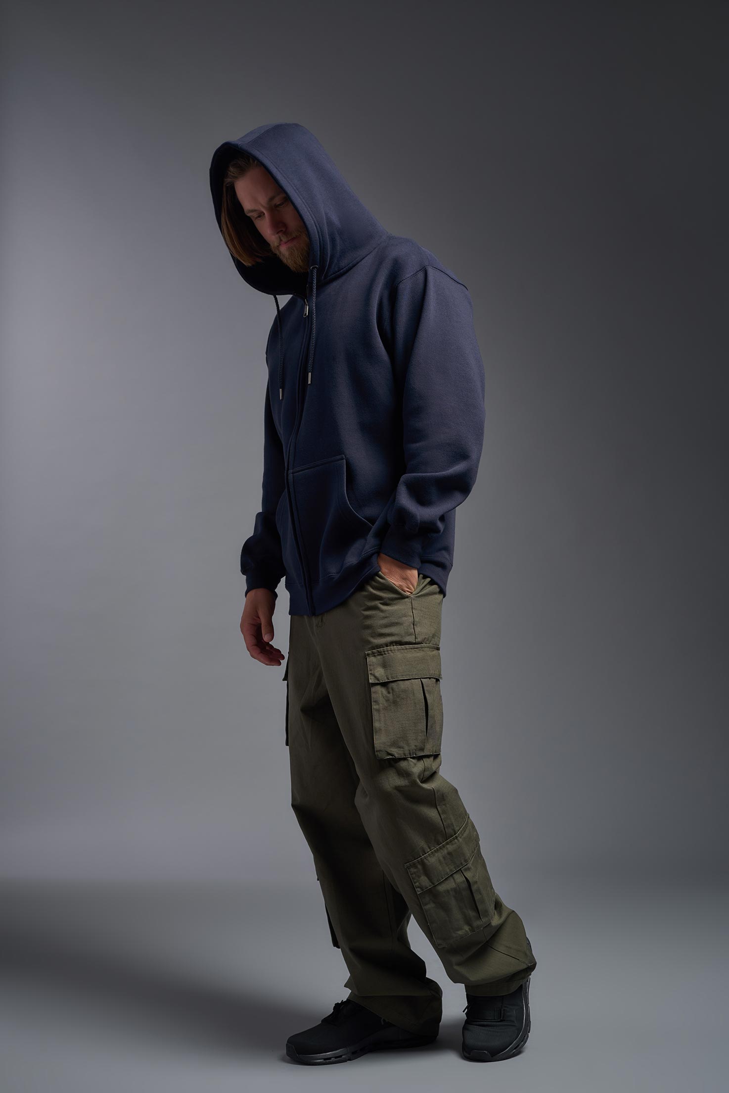 A male model wearing the unisex Americana 3-End Fleece Full Zip Hoodie in the color navy, made from 75% combed ring-spun USA-grown cotton and 25% polyester, showing the relaxed fit from a side view with hood up. This premium fleece hoodie is Made in the USA. #navy