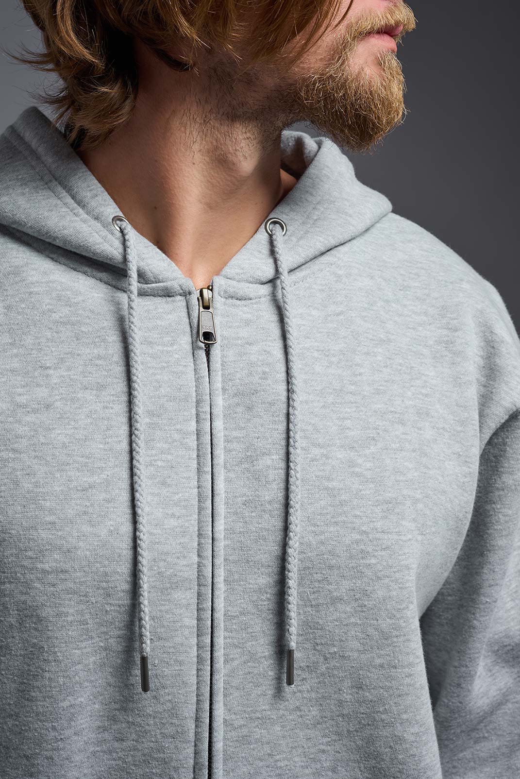 A male model wearing the unisex Americana 3-End Fleece Full Zip Hoodie in the color sport gray, made from 75% combed ring-spun USA-grown cotton and 25% polyester, showing the relaxed fit from a close-up collar view. This premium fleece hoodie is Made in the USA. #sport-gray