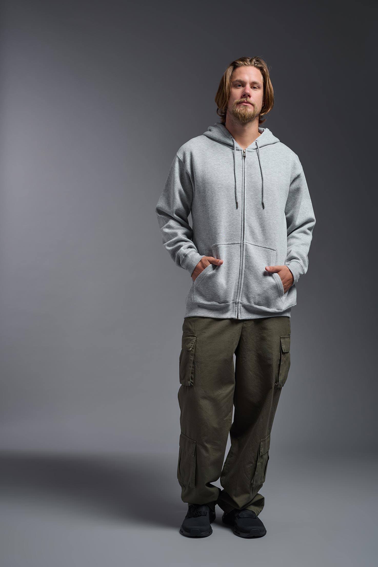 A male model wearing the unisex Americana 3-End Fleece Full Zip Hoodie in the color sport gray, made from 75% combed ring-spun USA-grown cotton and 25% polyester, showing the relaxed fit from a front view. This premium fleece hoodie is Made in the USA. #sport-gray
