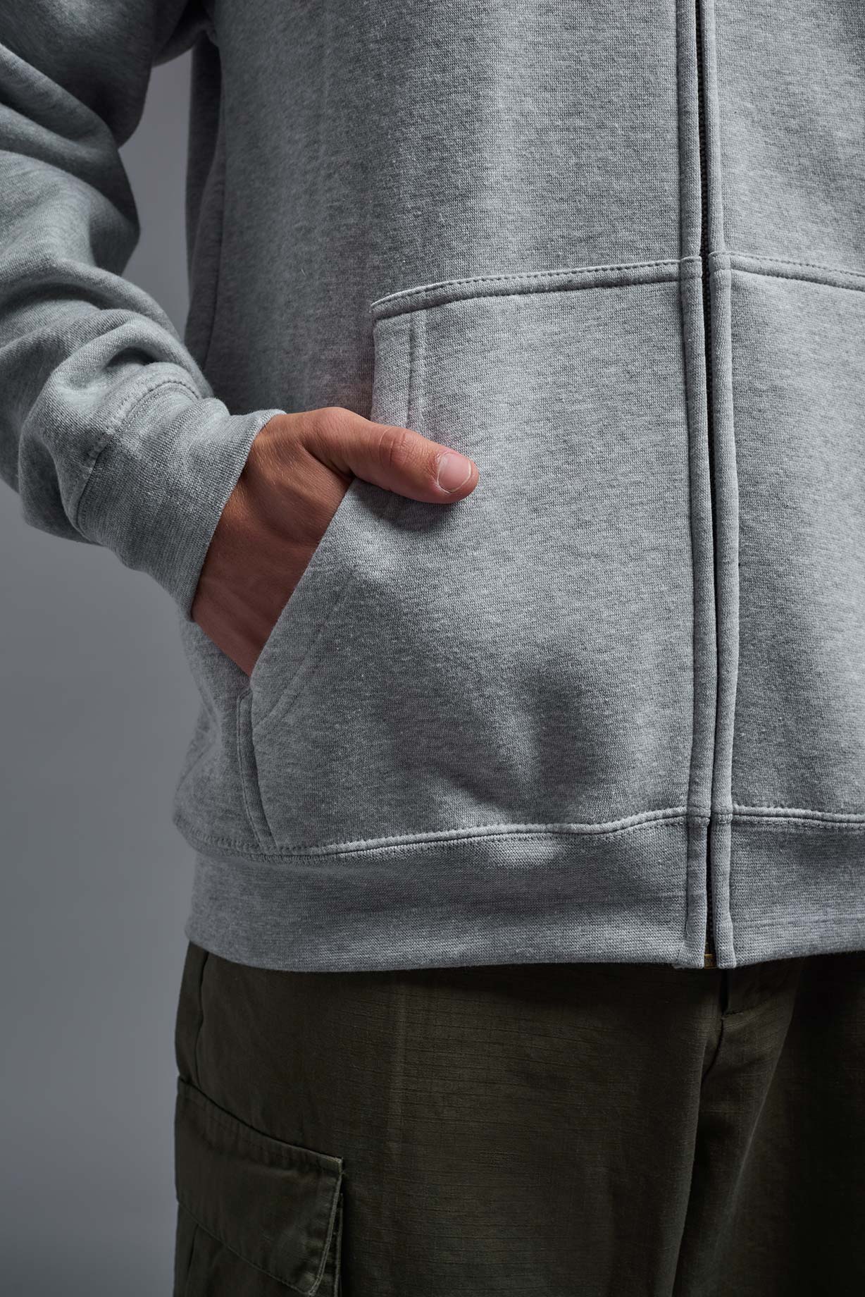 A male model wearing the unisex Americana 3-End Fleece Full Zip Hoodie in the color sport gray, made from 75% combed ring-spun USA-grown cotton and 25% polyester, showing the relaxed fit from a close-up pocket view. This premium fleece hoodie is Made in the USA. #sport-gray
