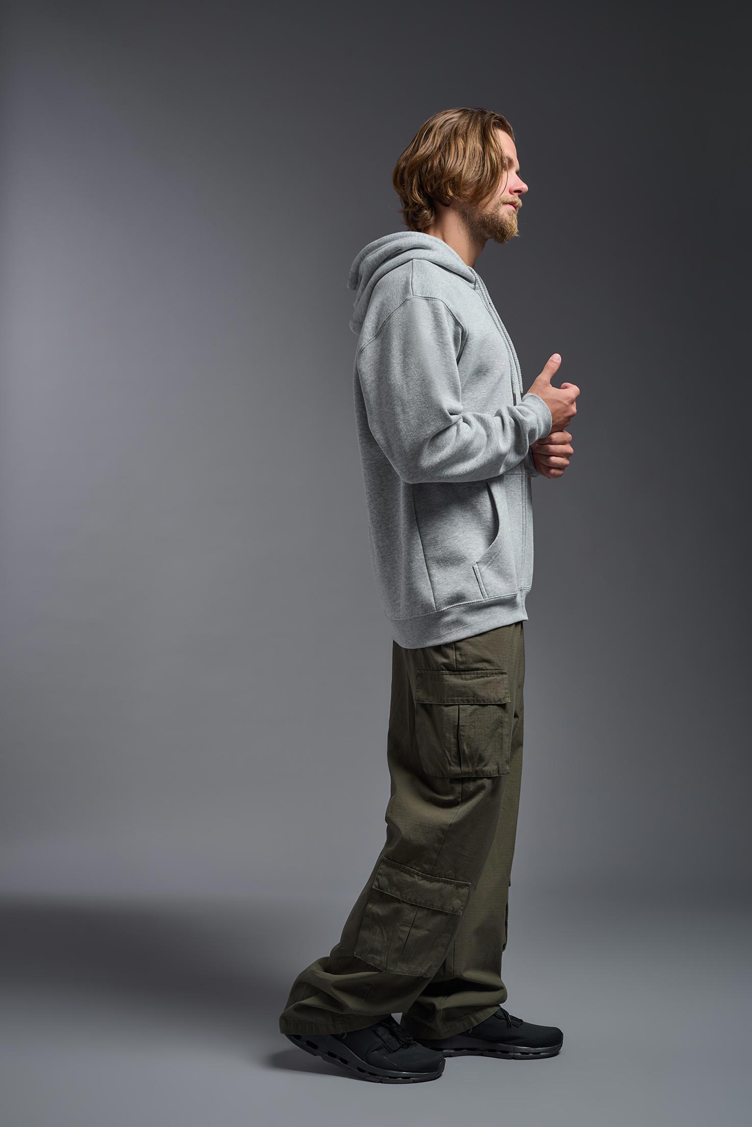 A male model wearing the unisex Americana 3-End Fleece Full Zip Hoodie in the color sport gray, made from 75% combed ring-spun USA-grown cotton and 25% polyester, showing the relaxed fit from a side view. This premium fleece hoodie is Made in the USA. #sport-gray