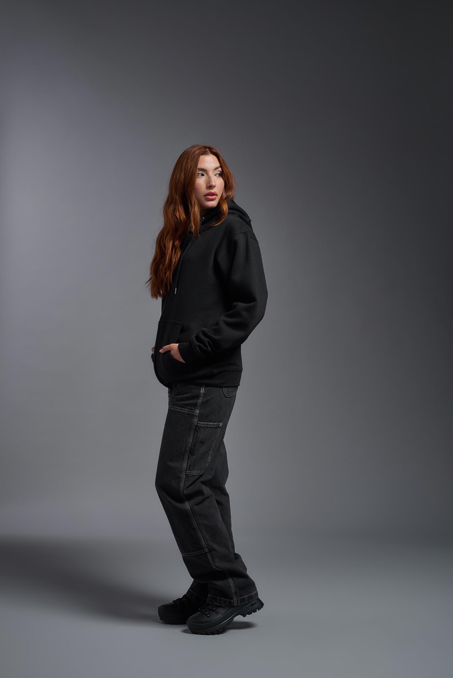 A female model wearing the unisex Americana 3-End Fleece Full Zip Hoodie in the color black, made from 75% combed ring-spun USA-grown cotton and 25% polyester, showing the relaxed fit from a side view. This premium fleece hoodie is Made in the USA. #black