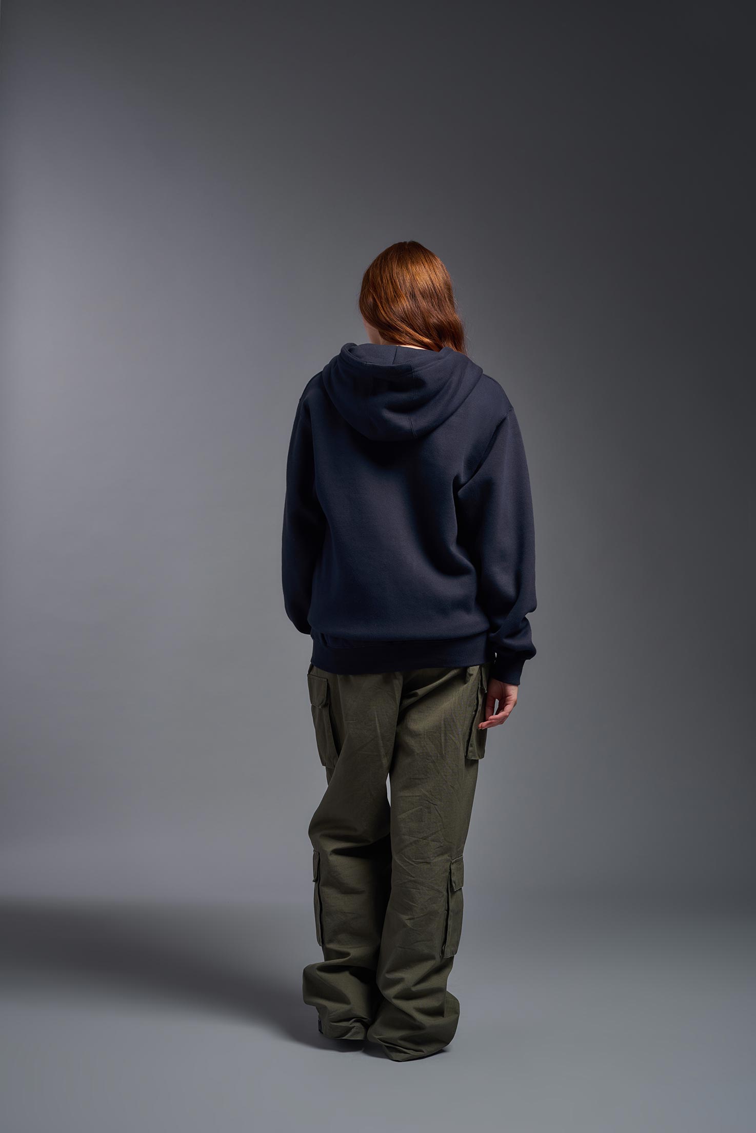 A female model wearing the unisex Americana 3-End Fleece Full Zip Hoodie in the color navy, made from 75% combed ring-spun USA-grown cotton and 25% polyester, showing the relaxed fit from a back view. This premium fleece hoodie is Made in the USA. #navy