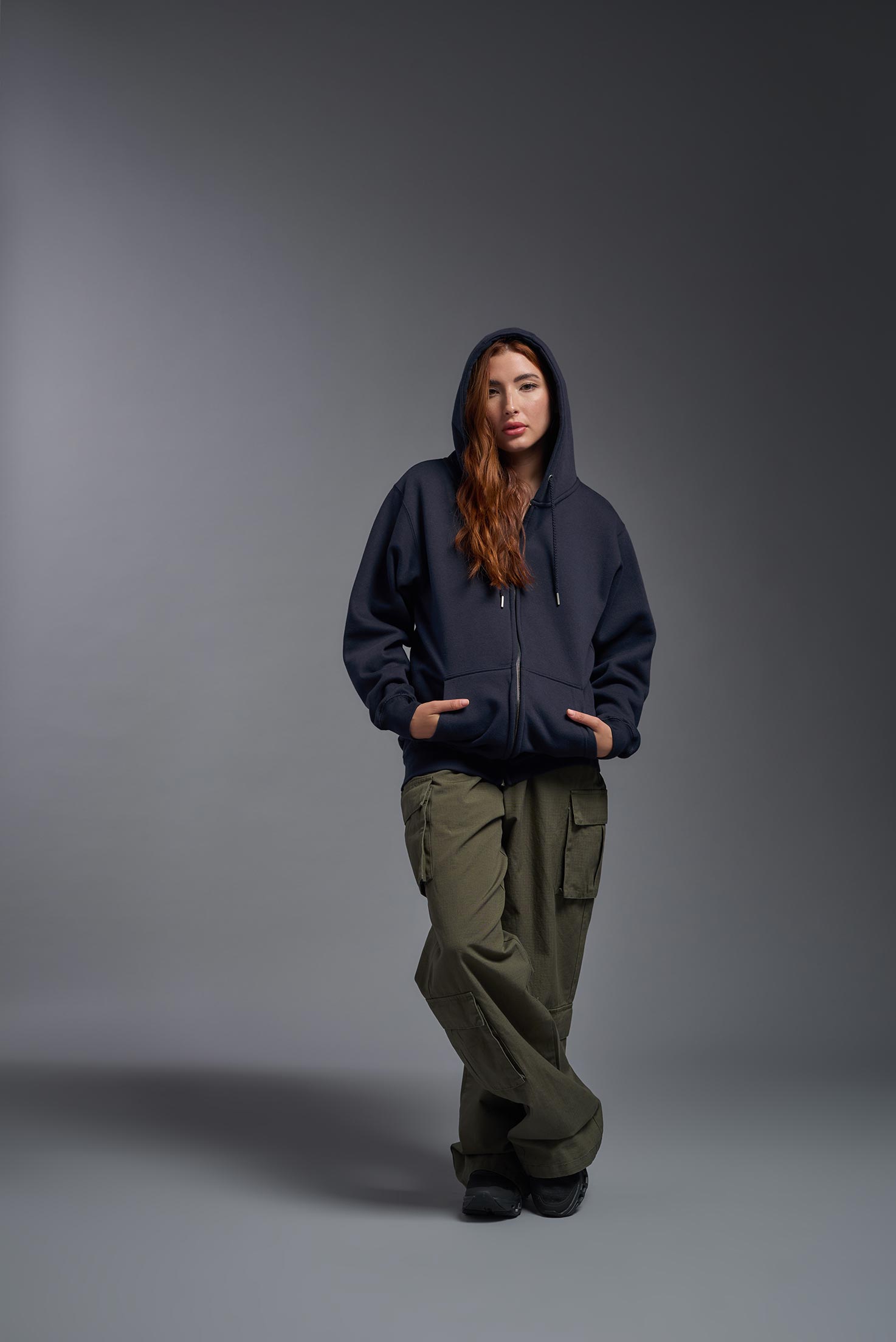 A female model wearing the unisex Americana 3-End Fleece Full Zip Hoodie in the color navy, made from 75% combed ring-spun USA-grown cotton and 25% polyester, showing the relaxed fit from a front view with hood up. This premium fleece hoodie is Made in the USA. #navy