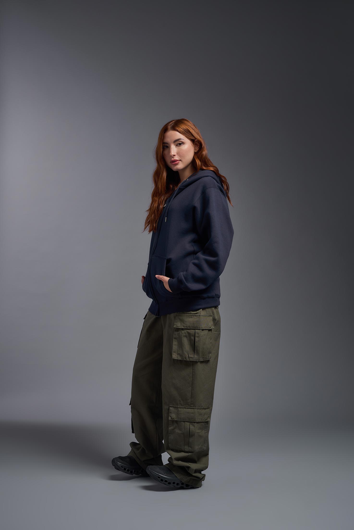 A female model wearing the unisex Americana 3-End Fleece Full Zip Hoodie in the color navy, made from 75% combed ring-spun USA-grown cotton and 25% polyester, showing the relaxed fit from a side view. This premium fleece hoodie is Made in the USA. #navy