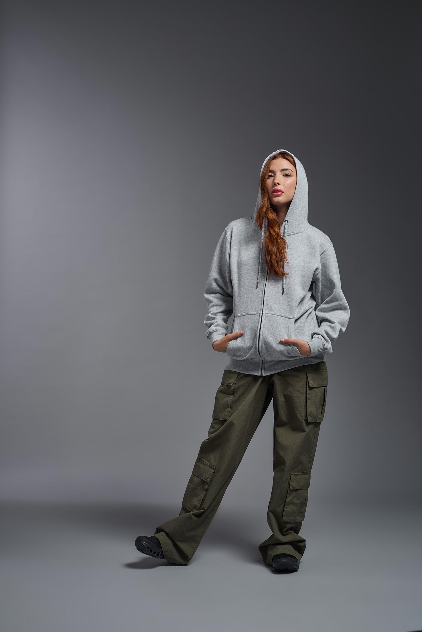 A female model wearing the unisex Americana 3-End Fleece Full Zip Hoodie in the color sport gray, made from 75% combed ring-spun USA-grown cotton and 25% polyester, showing the relaxed fit from a front view with hood up. This premium fleece hoodie is Made in the USA. #sport-gray