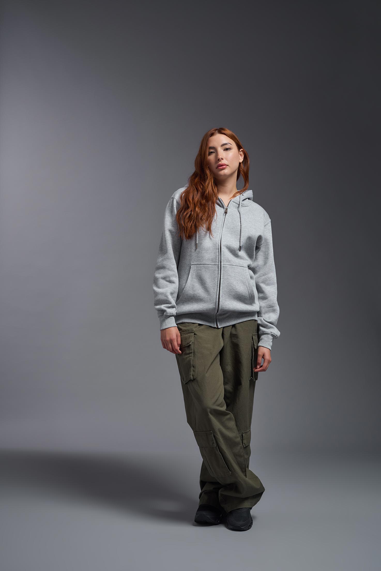 A female model wearing the unisex Americana 3-End Fleece Full Zip Hoodie in the color sport gray, made from 75% combed ring-spun USA-grown cotton and 25% polyester, showing the relaxed fit from a front view. This premium fleece hoodie is Made in the USA. #sport-gray
