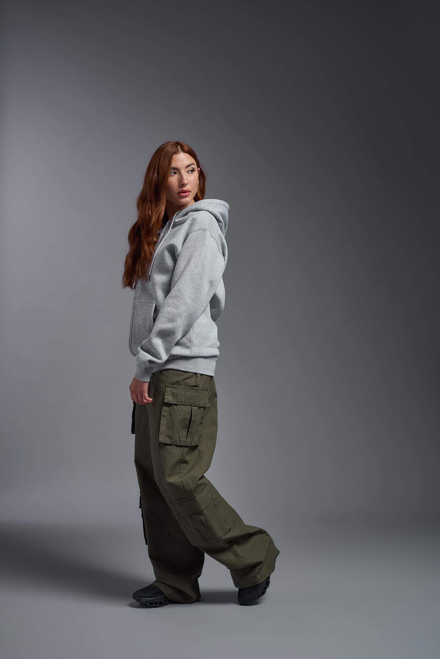 A female model wearing the unisex Americana 3-End Fleece Full Zip Hoodie in the color sport gray, made from 75% combed ring-spun USA-grown cotton and 25% polyester, showing the relaxed fit from a side view. This premium fleece hoodie is Made in the USA. #sport-gray