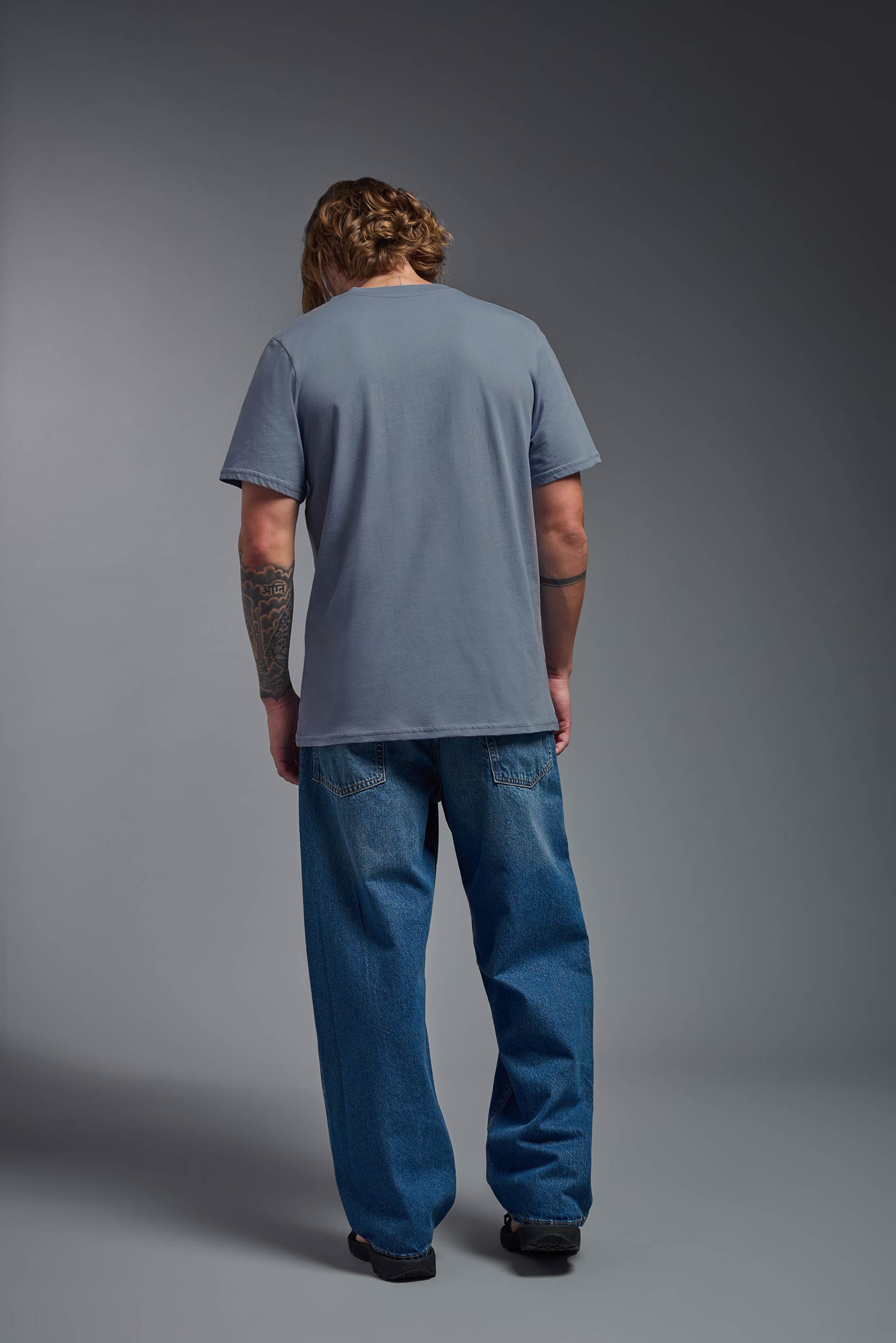 A male model wearing the unisex Organic Soft Cotton T-shirt in the color canyon blue, made in the USA from 100% GOTS certified organic cotton from a back view. This shirt is unisex, made in the USA, and perfect for bulk screen printing and decorating. #canyon-blue