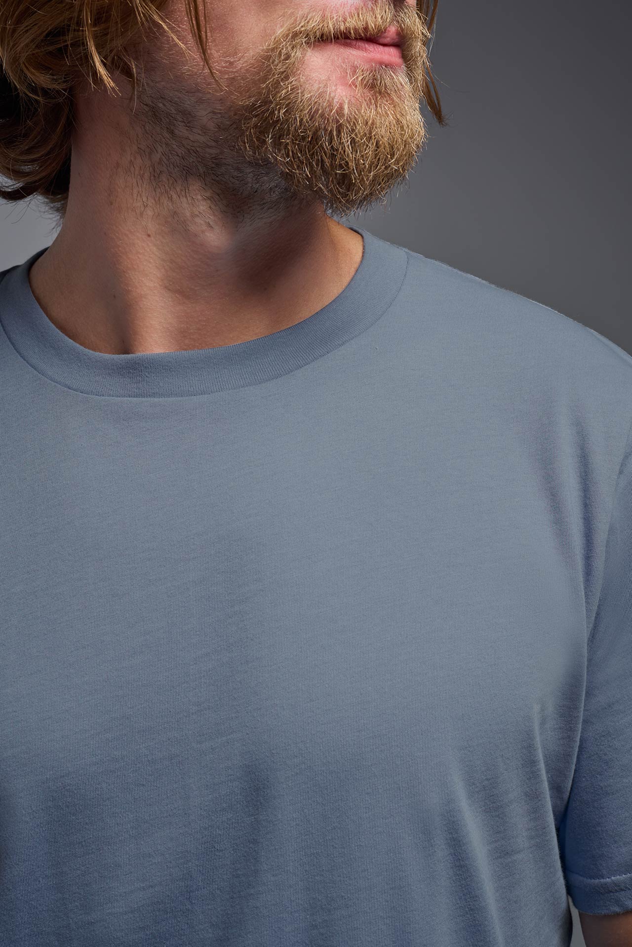 A male model wearing the unisex Organic Soft Cotton T-shirt in the color canyon blue, made in the USA from 100% GOTS certified organic cotton from a closeup collar front view. This shirt is unisex, made in the USA, and perfect for bulk screen printing and decorating. #canyon-blue