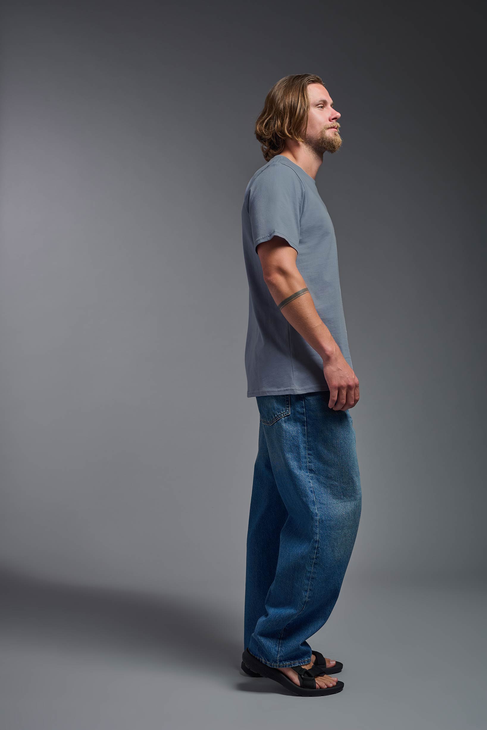 A male model wearing the unisex Organic Soft Cotton T-shirt in the color canyon blue, made in the USA from 100% GOTS certified organic cotton from a side view. This shirt is unisex, made in the USA, and perfect for bulk screen printing and decorating. #canyon-blue