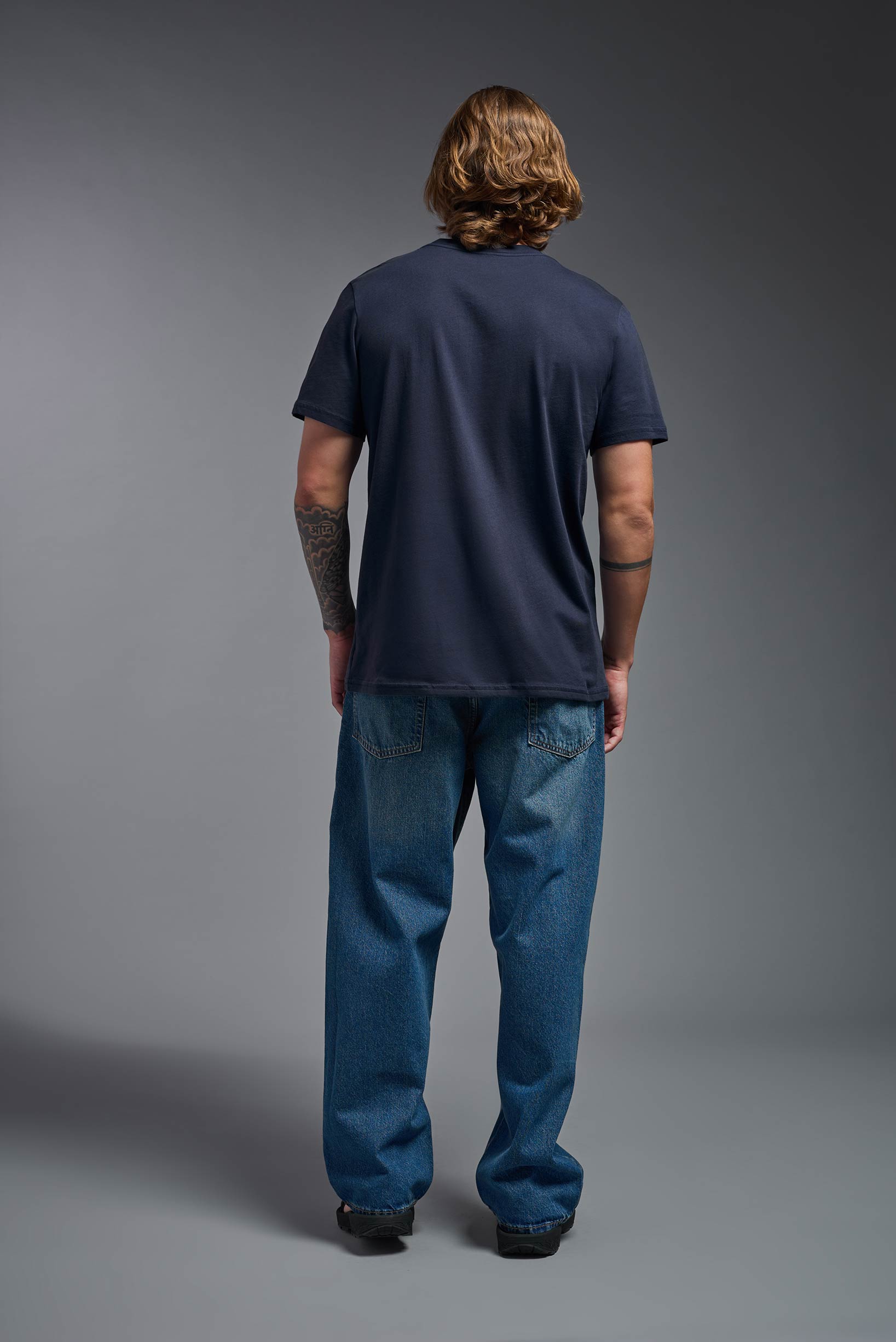 A male model wearing the unisex Organic Soft Cotton T-shirt in the color nova, made from 100% GOTS certified organic cotton from a full body back view. This shirt is unisex, made in the USA, and perfect for bulk screen printing and decorating. #nova