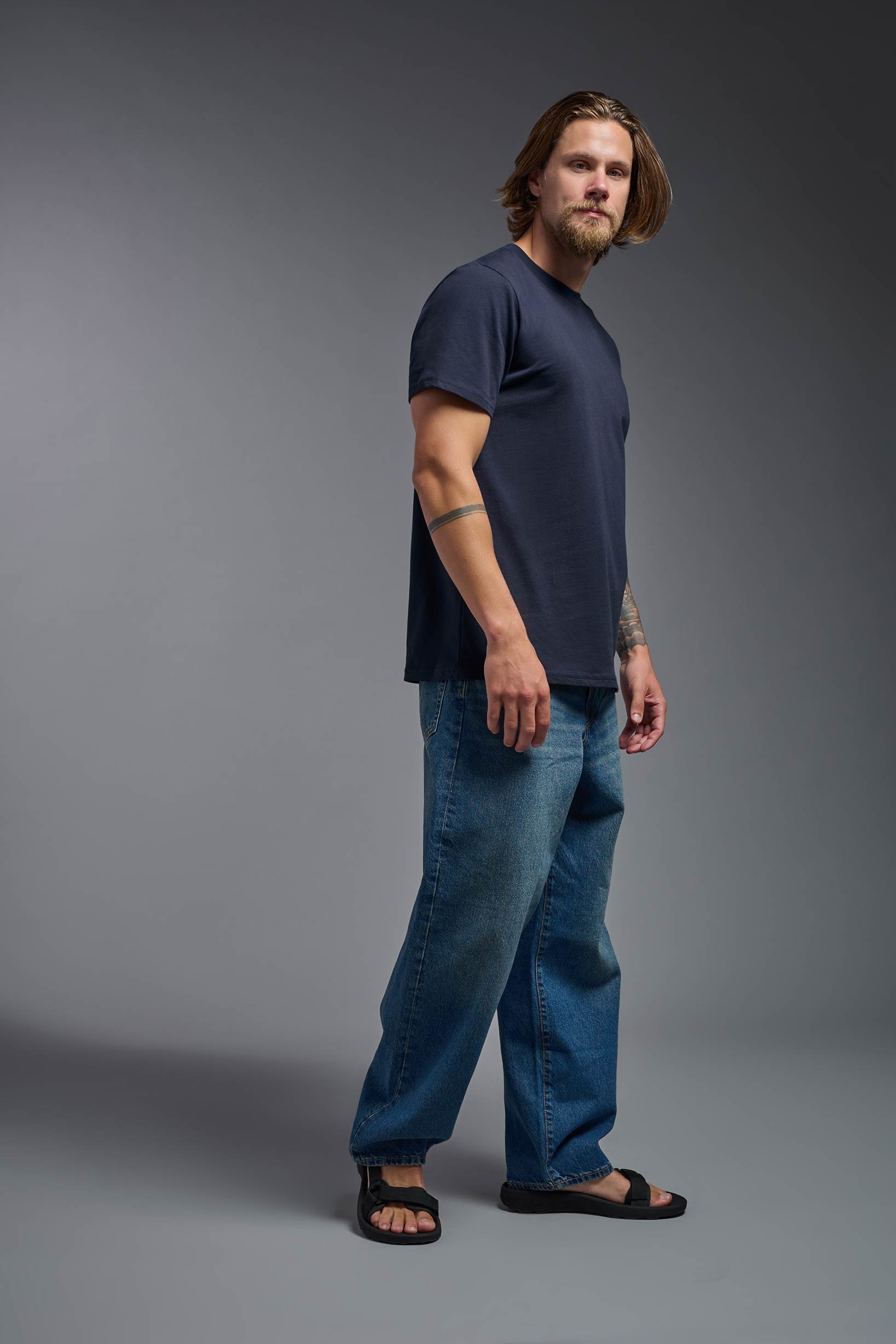 A male model wearing the unisex Organic Soft Cotton T-shirt in the color nova, made from 100% GOTS certified organic cotton from a full body side view. This shirt is unisex, made in the USA, and perfect for bulk screen printing and decorating. #nova