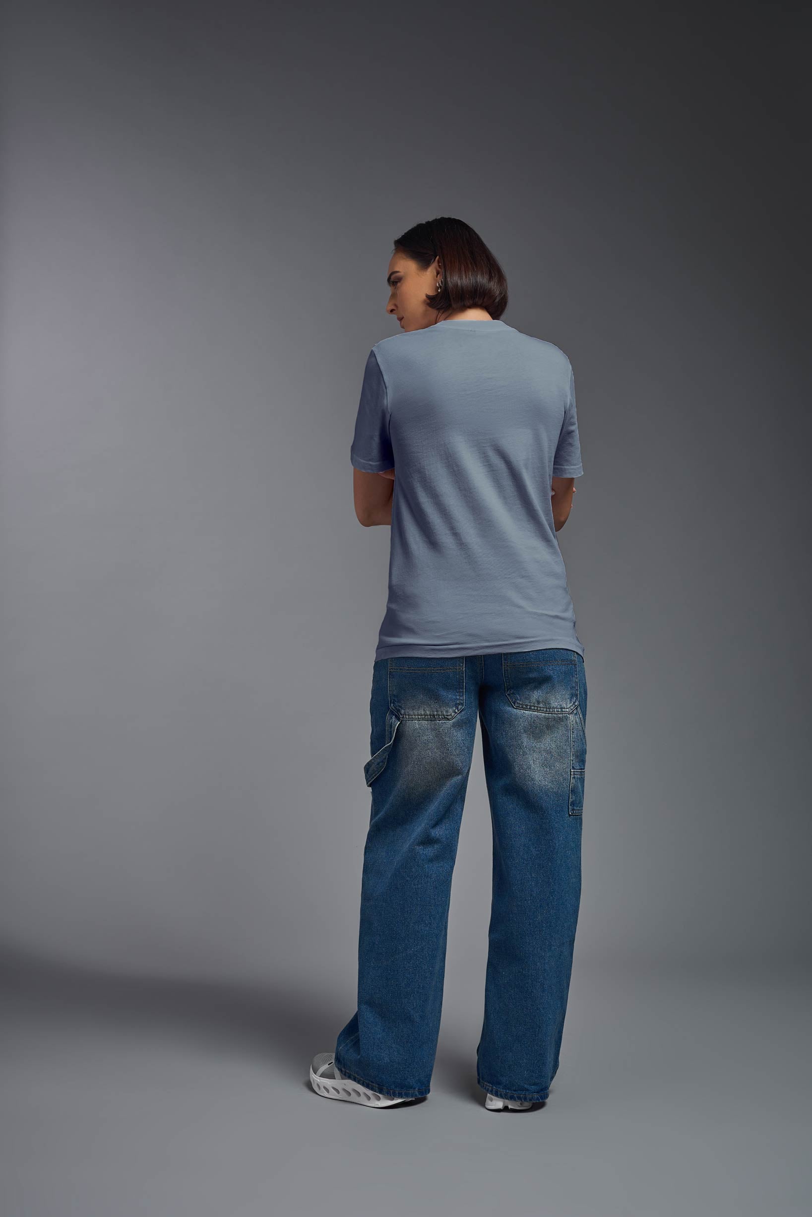 A female model wearing the unisex Organic Soft Cotton T-shirt in the color canyon blue, made in the USA from 100% GOTS certified organic cotton from a full body back view. This shirt is unisex, made in the USA, and perfect for bulk screen printing and decorating. #canyon-blue