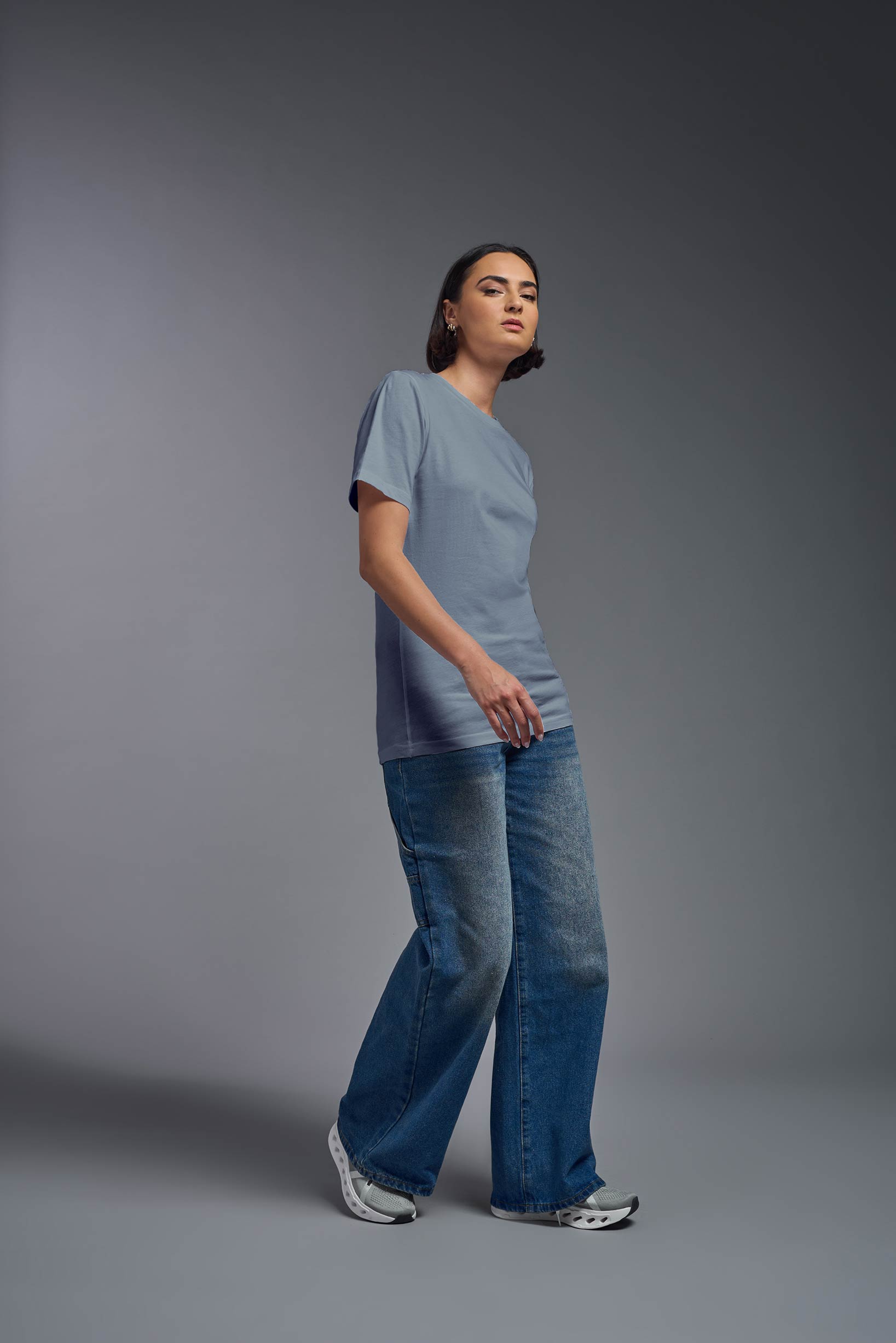 A female model wearing the unisex Organic Soft Cotton T-shirt in the color canyon blue, made in the USA from 100% GOTS certified organic cotton from a full body side view. This shirt is unisex, made in the USA, and perfect for bulk screen printing and decorating. #canyon-blue