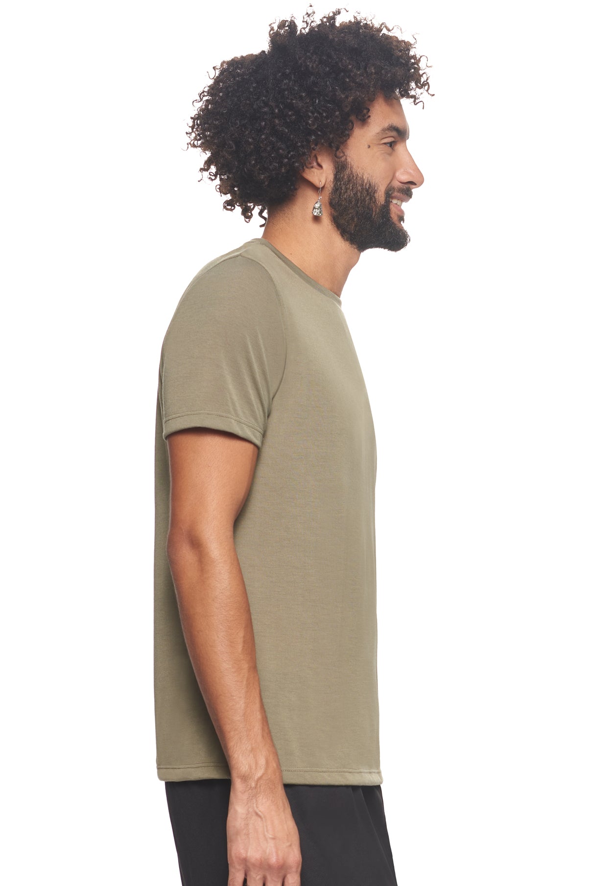 A male model with curly hair wearing the men's Siro™ Crewneck Tee in the color olive, made from 100% filament polyester technology, showing the modern fit from a side view. This shirt is elevated and fashion forward while also offering quick-drying and moisture-wicking performance. It is made in the USA, and available for bulk purchase. #olive