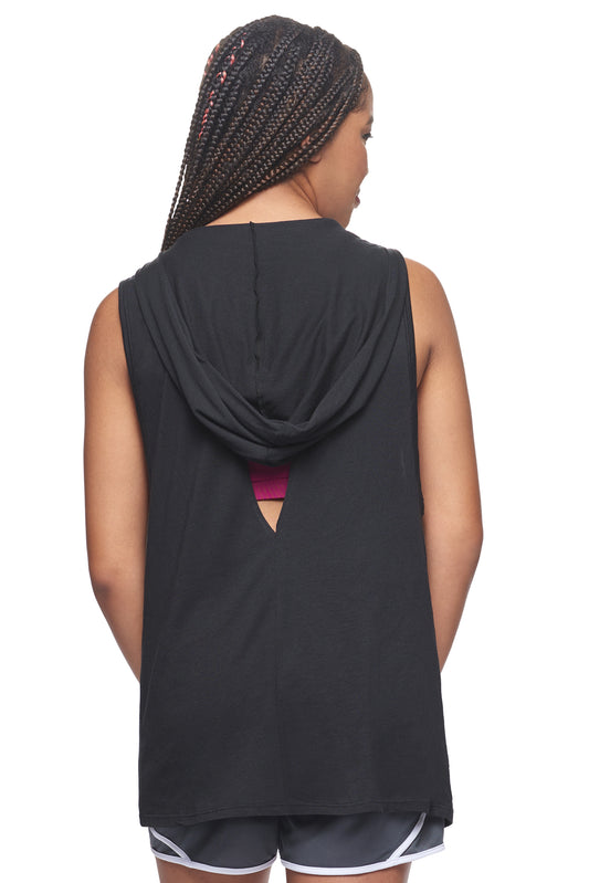 A female model with braided hair wearing the women's MoCA Sleeveless Hoodie  in the color black, made from a luxurious blend of 50% LENZING Modal and 50% Combed Ring-Spun Cotton, showing the relaxed fit from a back view, hood down. This hoodie tank shirt is elevated, eco-friendly, made in the USA, and available for bulk purchase. #black