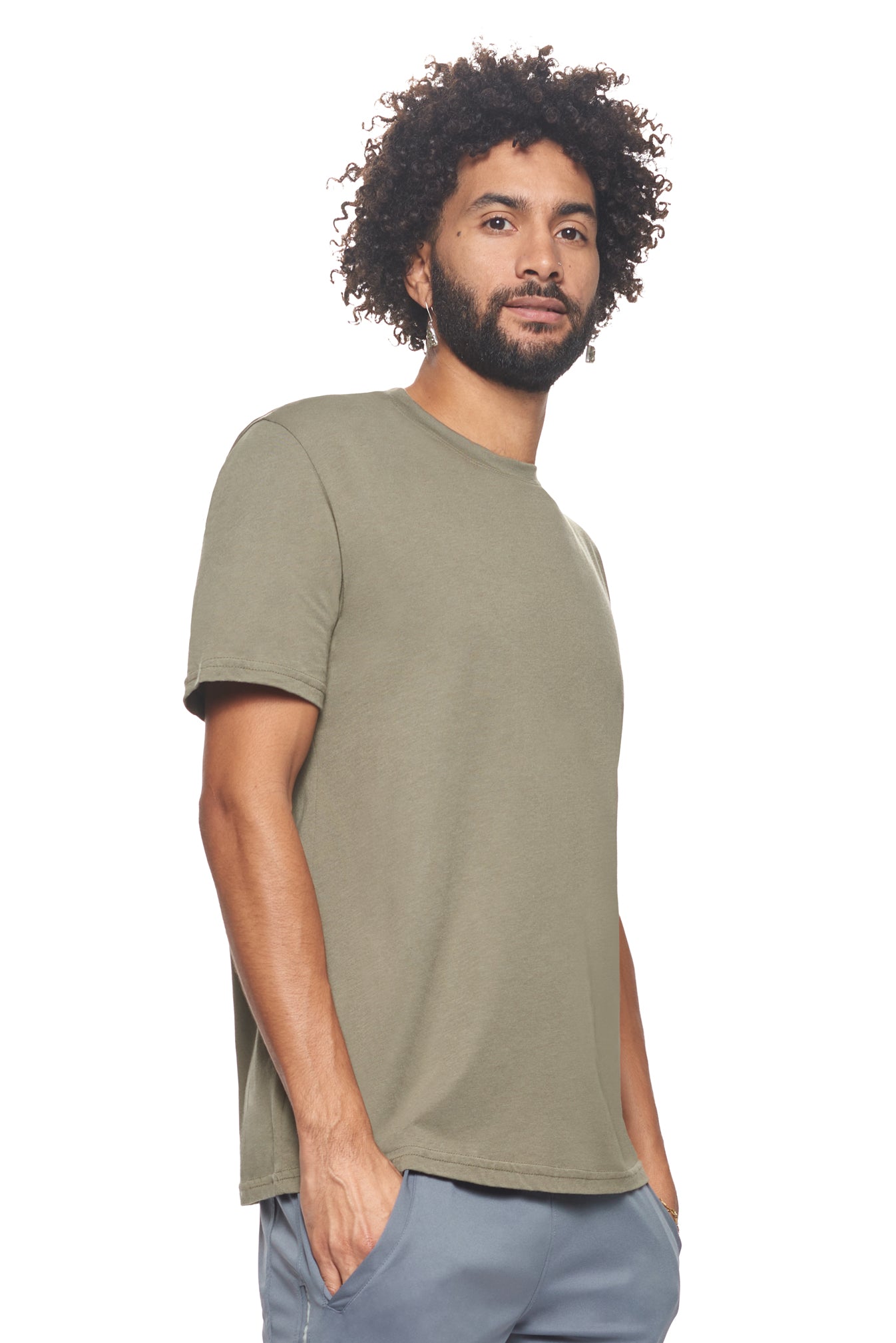 A male model with curly hair wearing the Men's MoCA V-Neck Tee in the color olive, made from a luxurious blend of 50% LENZING Modal and 50% Combed Ring-Spun Cotton, showing the relaxed fit from a side view. This fashion-forward, more sustainable t-shirt is elevated, eco-friendly, made in the USA, and available for bulk purchase. #olive