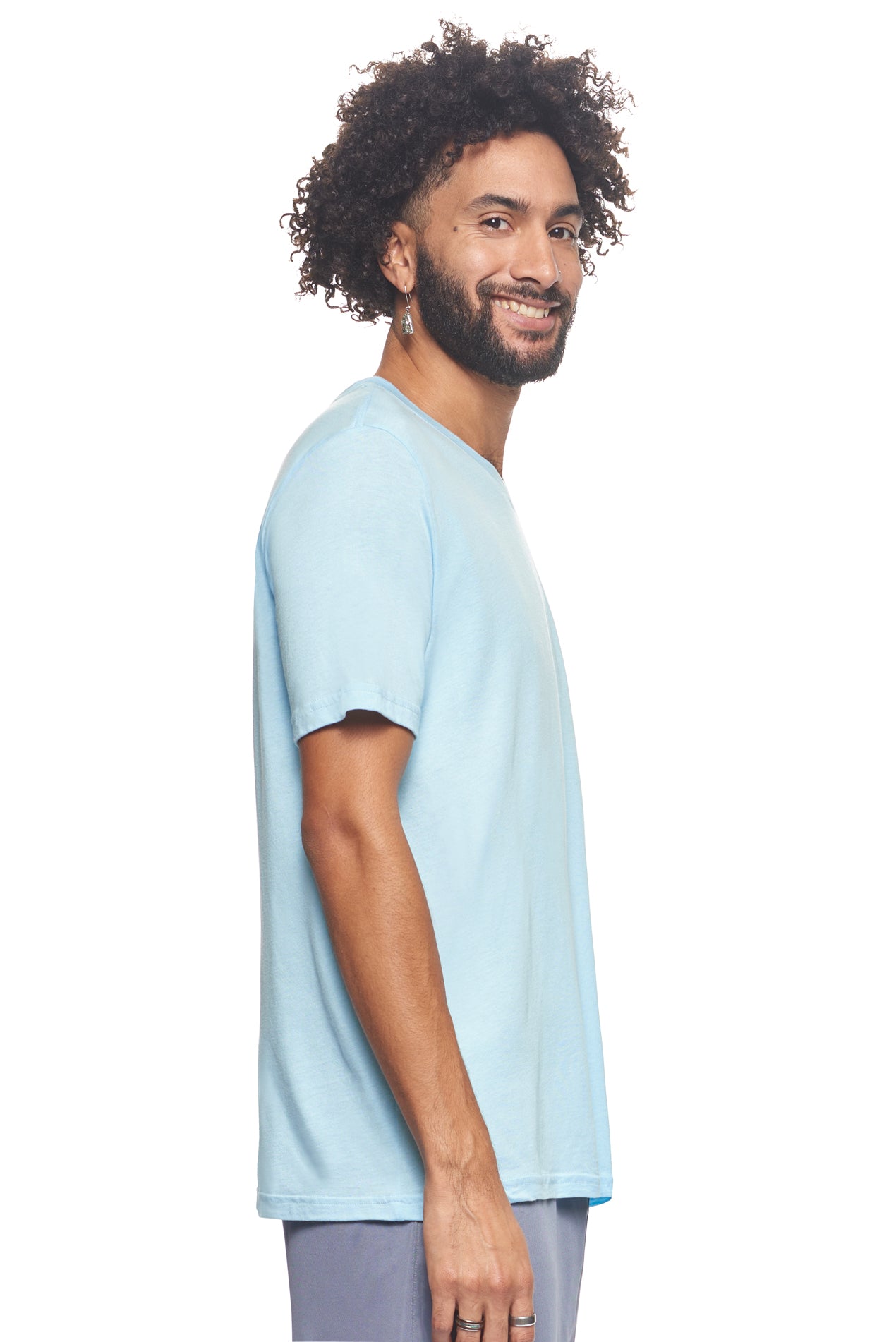A male model with curly hair wearing the Men's MoCA V-Neck Tee in the color light blue, made from a luxurious blend of 50% LENZING Modal and 50% Combed Ring-Spun Cotton, showing the relaxed fit from a side view. This fashion-forward, more sustainable t-shirt is elevated, eco-friendly, made in the USA, and available for bulk purchase. #light-blue