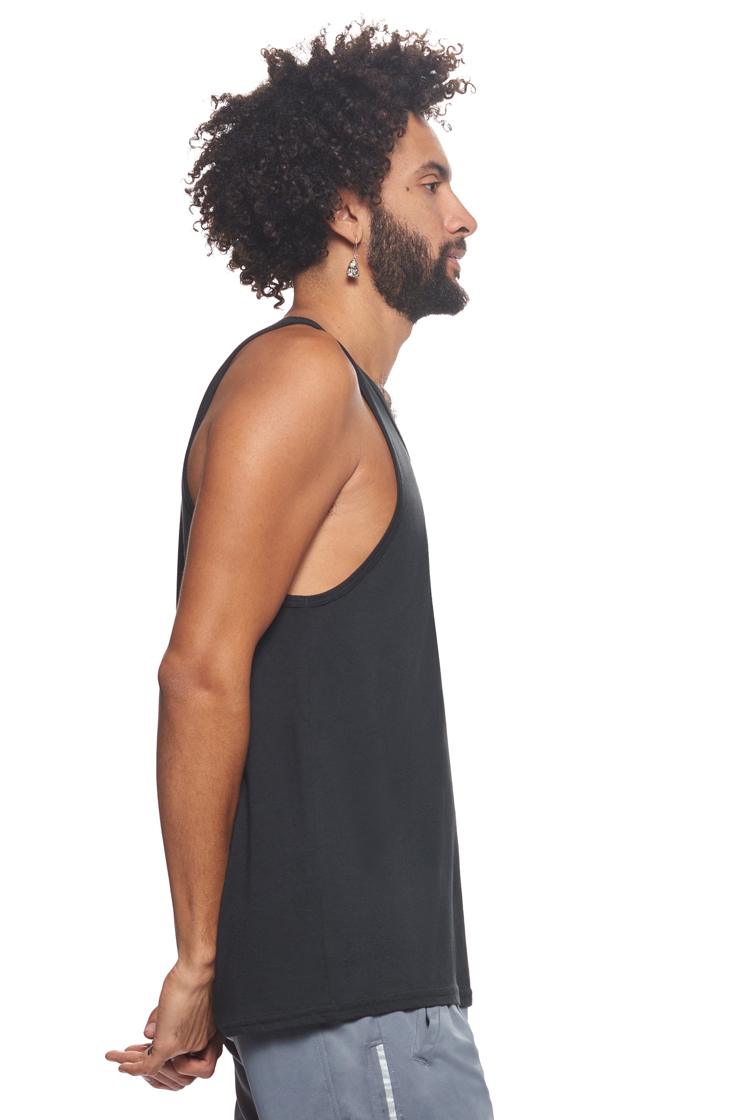 A male model with curly hair wearing the men's MoCA Sleeveless Tank in the color black, made from a luxurious blend of 50% LENZING Modal and 50% Combed Ring-Spun Cotton, showing the relaxed fit from a side view. This tank is elevated, eco-friendly, made in the USA, and available for bulk purchase. #black