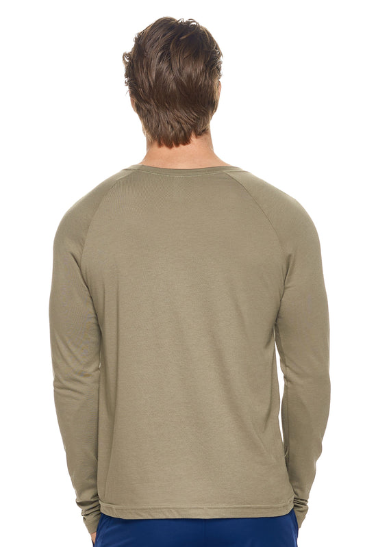 A male model with dirty blonde hair wearing the men's MoCA Long Sleeve Raglan Tee in the color olive, made from a luxurious blend of 50% LENZING Modal and 50% Combed Ring-Spun Cotton, showing the relaxed fit from a back view. This shirt is elevated, eco-friendly, made in the USA, and available for bulk purchase. #olive