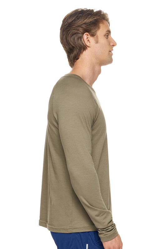 A male model with dirty blonde hair wearing the men's MoCA Long Sleeve Raglan Tee in the color olive, made from a luxurious blend of 50% LENZING Modal and 50% Combed Ring-Spun Cotton, showing the relaxed fit from a side view. This shirt is elevated, eco-friendly, made in the USA, and available for bulk purchase. #olive